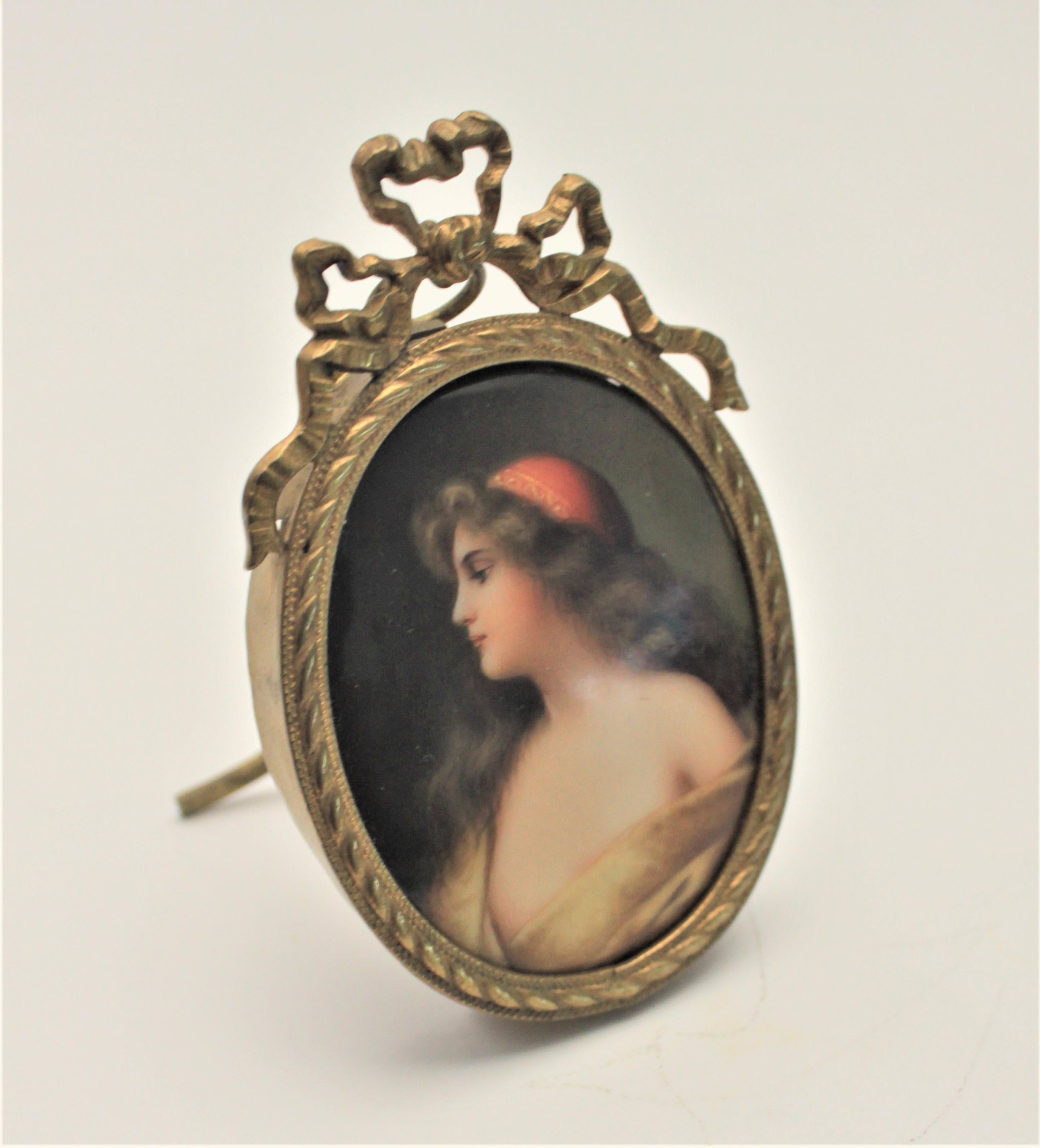 This antique hand painted miniature portrait on porcelain is unsigned and unmarked, but presumed to have been made in France in approximately the 1880s. The portrait depicts a young woman and is framed in a period brass frame with a French ribbon