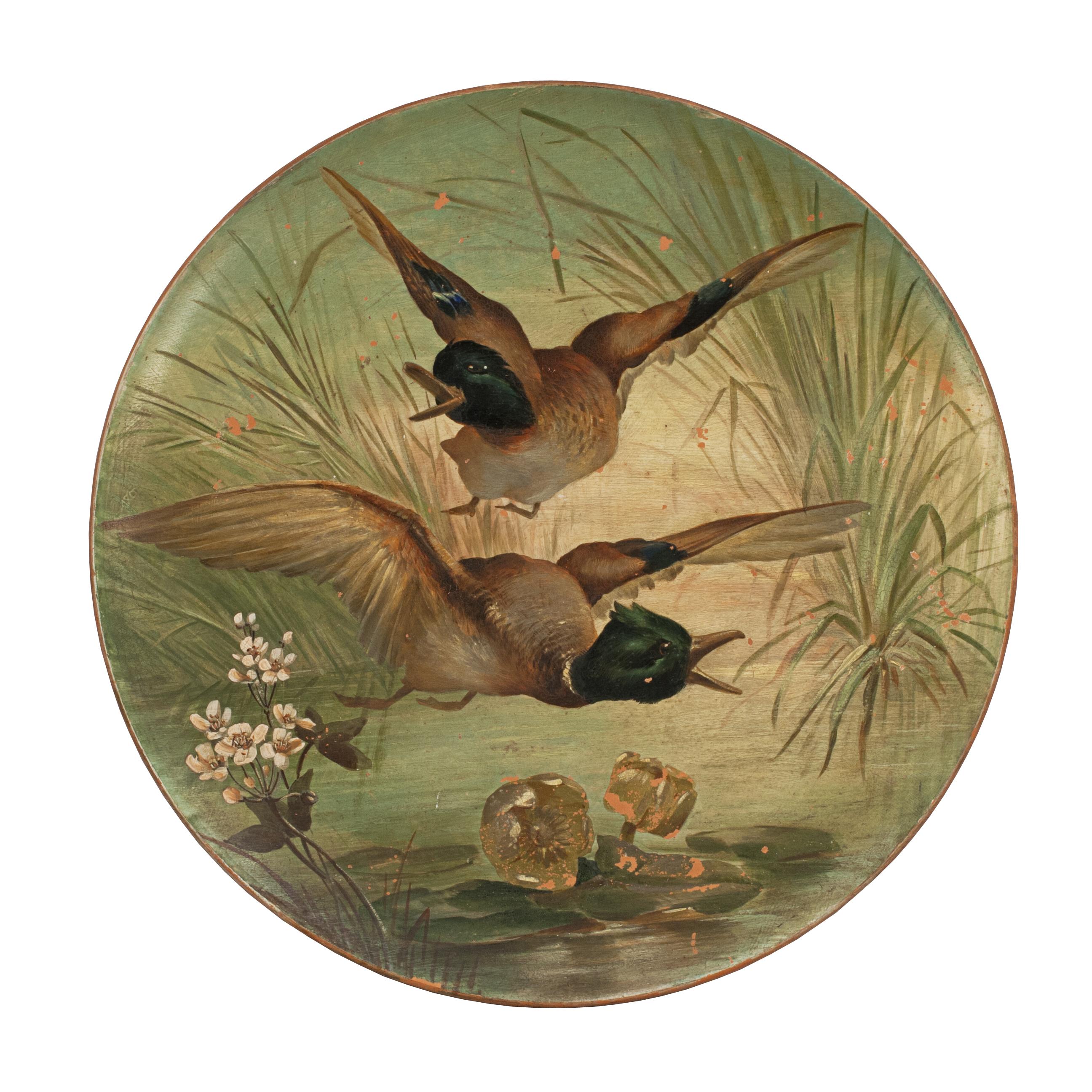 A large pair of terracotta plaques / plates. Each plate is hand painted with a different waterfowl scene. One depicts three swans being attacked by two birds of prey, whilst the other depicts two male mallard ducks in flight. The painter and maker