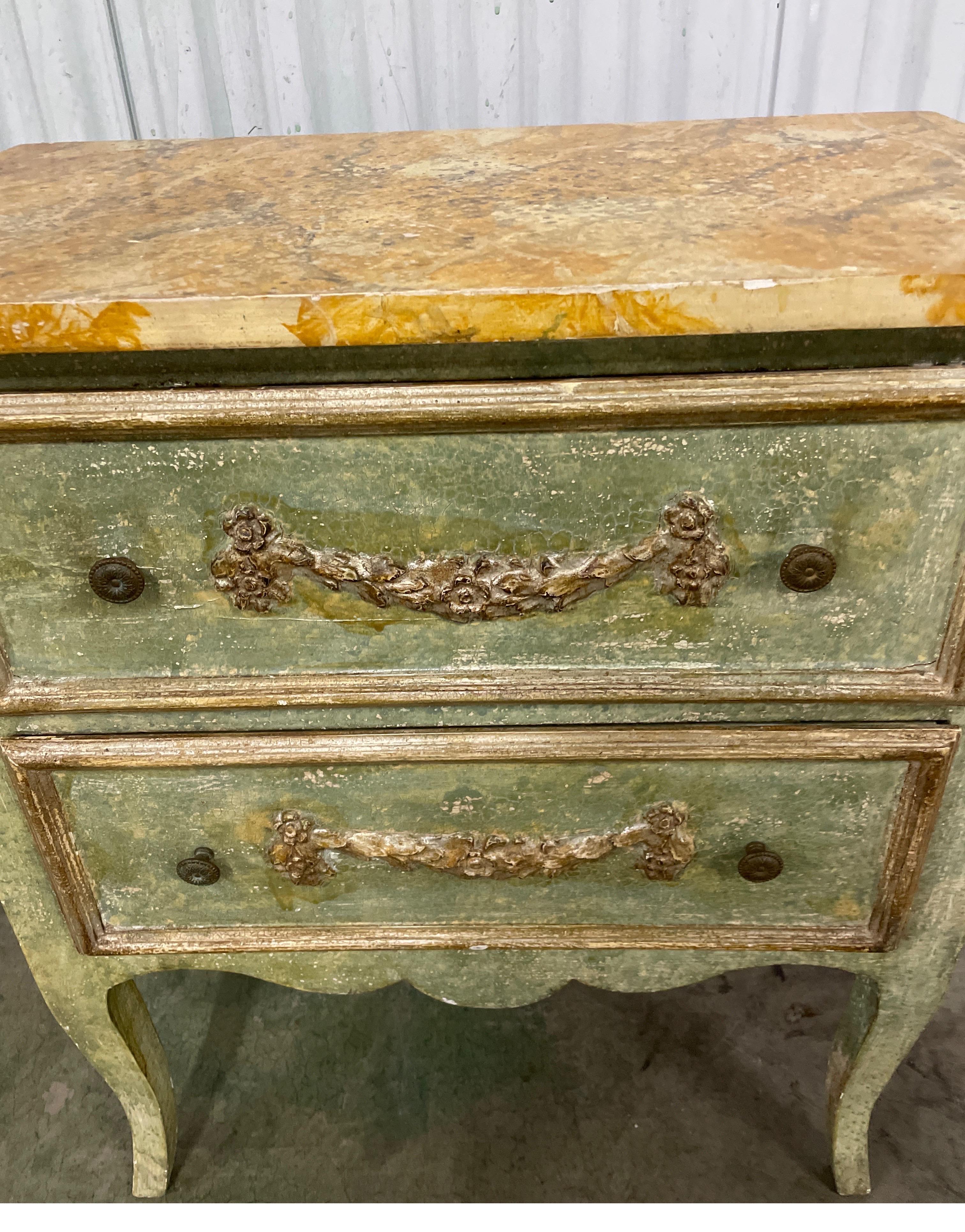Commode italienne vintage de style néoclassique peinte à la main à deux tiroirs avec dessus en faux marbre. Chaque tiroir est orné d'une guirlande en bois sculpté et les côtés sont ornés d'une urne sculptée. Les tiroirs sont tapissés de papier