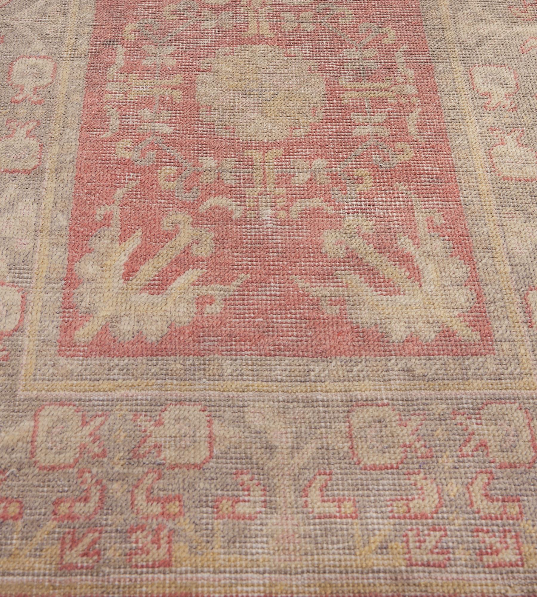 This antique, circa 1900, Khotan runner has a shaded coral-red field with a central column of golden-yellow palmettes and vase motifs surrounded by an angular floral band and a pair of bold flowerheads in each corner, an inner light-grey floral vine