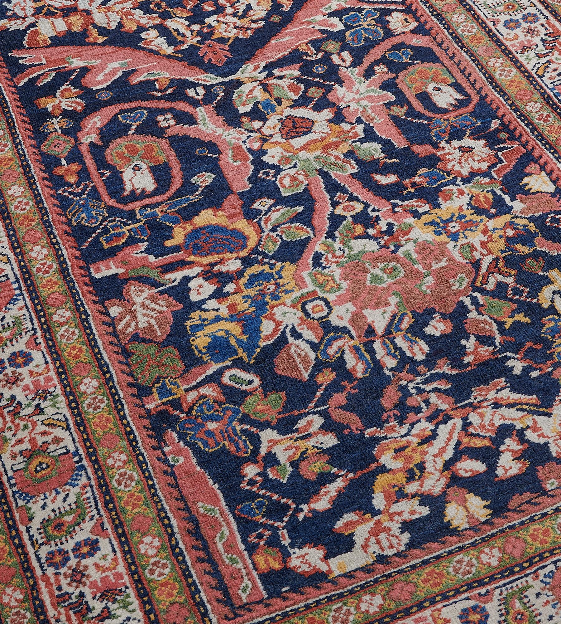 This antique handwoven Sultanabad runner has a deep indigo-blue field with an overall design of brick-red angular acanthus leaves supporting a large brick-red flower head surrounded by a light blue garland further stylized floral vine and smaller