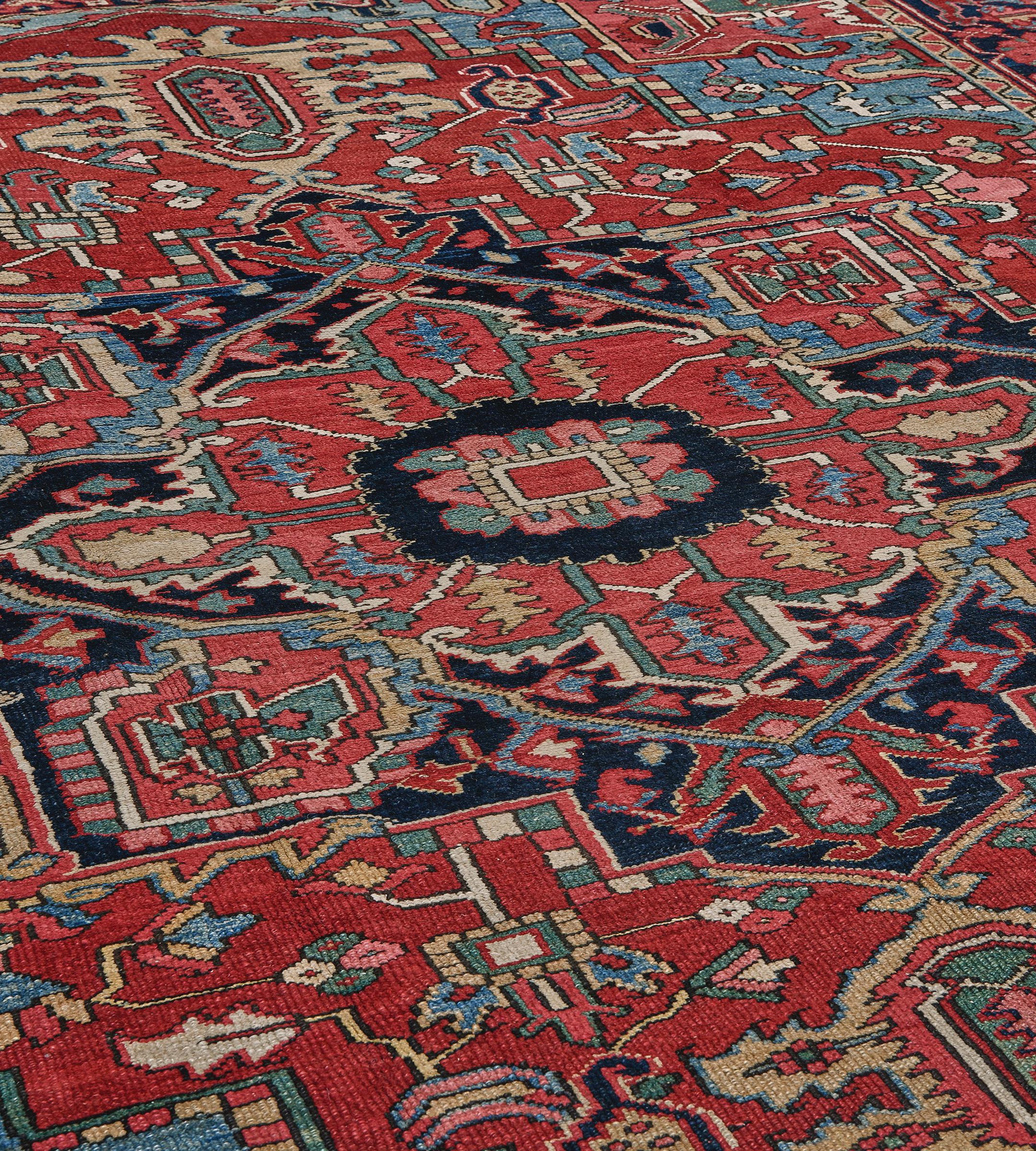 This traditional handwoven Persian Heriz Serapi rug has a brick red field of whimsical geometric floral sprays enclosing a deep indigo imperial medallion and in soft shaded blue spandrels of similar geometry, in a deep indigo linked turtle-palmette
