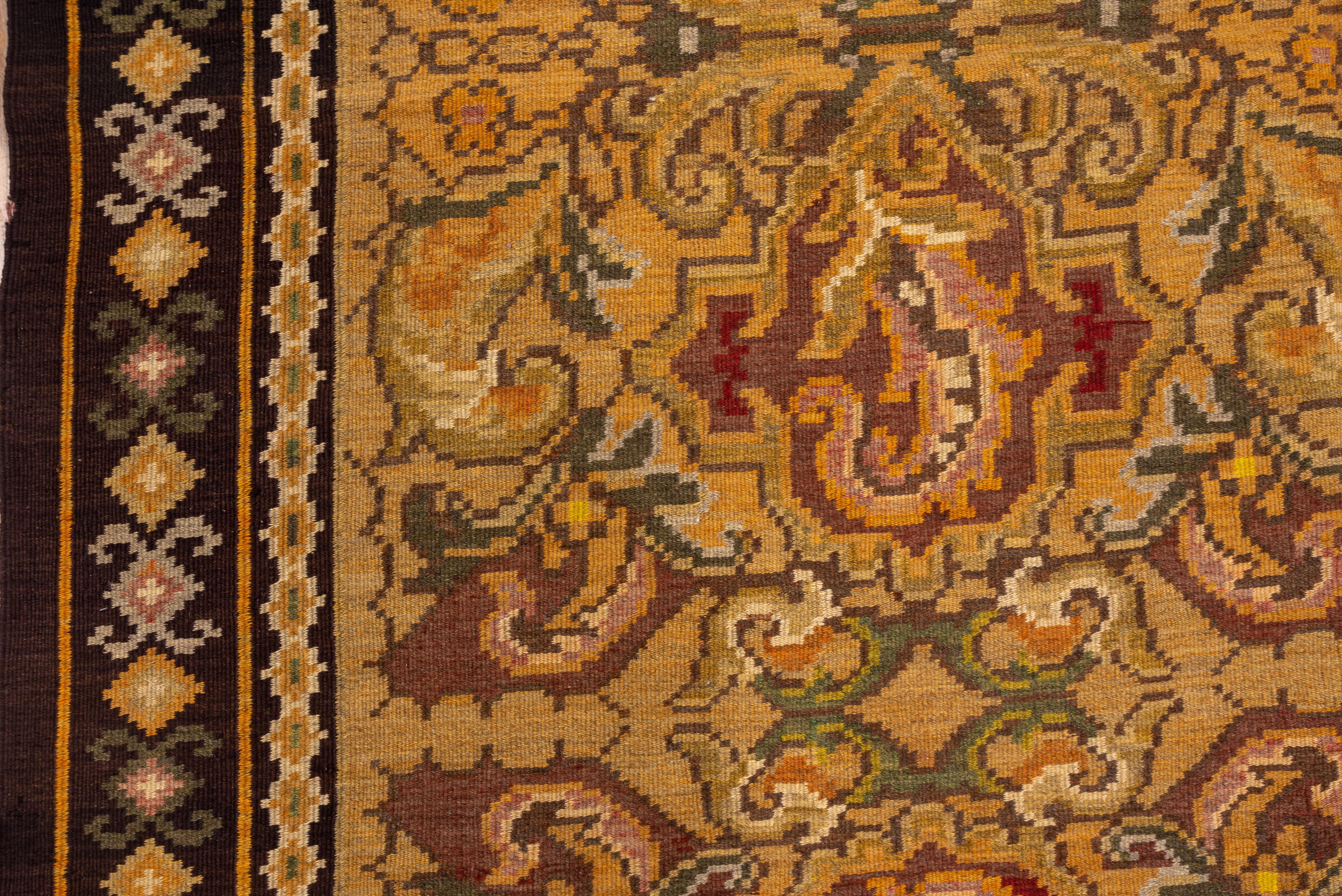 Ce tapis en tapisserie kilim de Russie méridionale présente un champ de couleur beige doré avec un motif en trois échelons de cartouches et de formes de feuilles barbelées détaillées dans les tons sienne, crème et saumon. Bordure en terre de Sienne