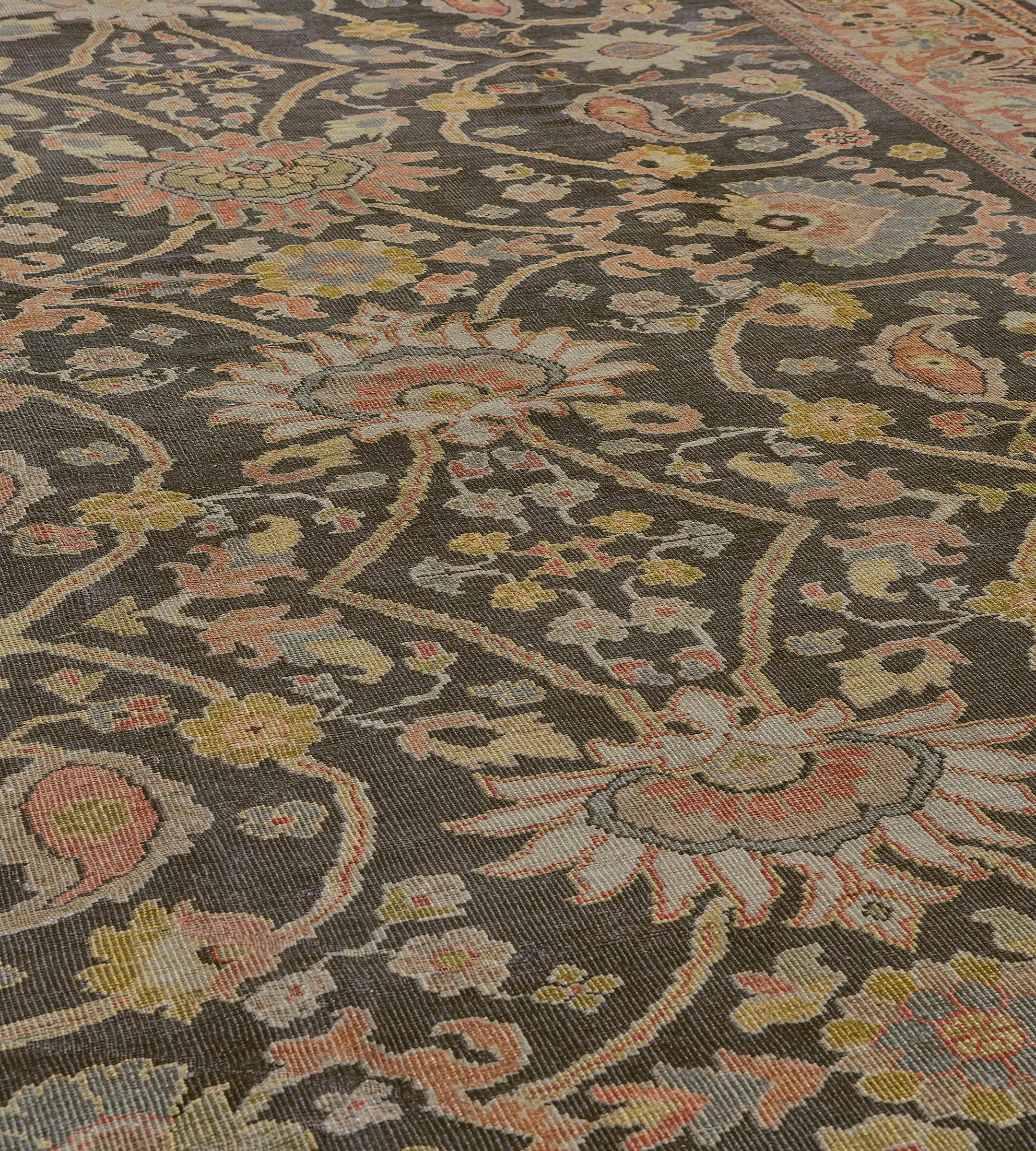 This traditional hand-woven Persian Sultanabad rug has a dusty charcoal field with overall design of bold palmettes issuing scrolling floral and paisley motif, in a broad coral meandering palmette border between delicate golden stripes.