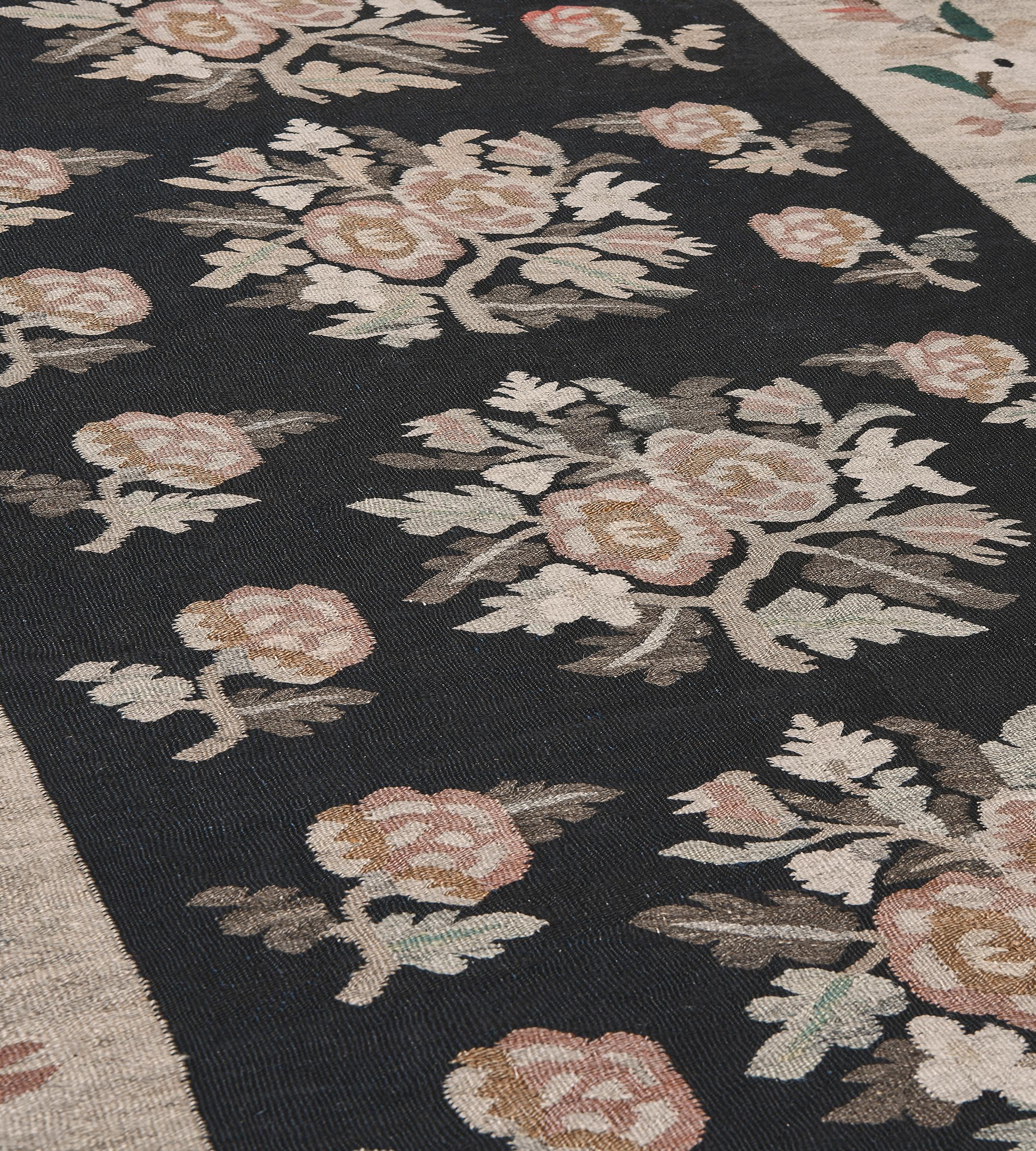 This traditional handwoven Romanian Bessarabian rug has a charcoal-black field with diagonal rows of polychrome floral sprays, in a whimsical sandy-ivory border of angular meandering flowering vines.