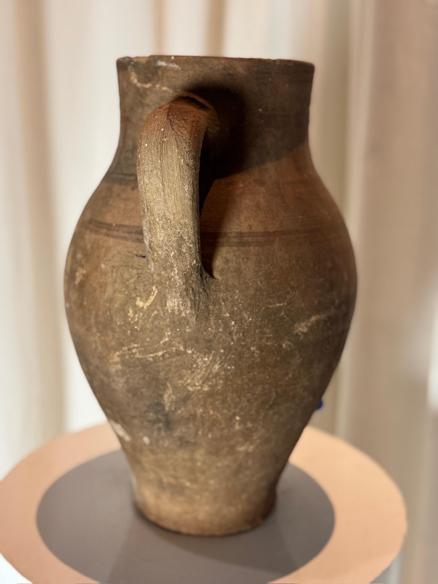 This exquisite antique terracotta water jug is a testament to the beauty of traditional craftsmanship. Hand-formed and kiln-fired, this earthenware vessel showcases a gracefully curved body with a sturdy handle, designed for both aesthetic appeal