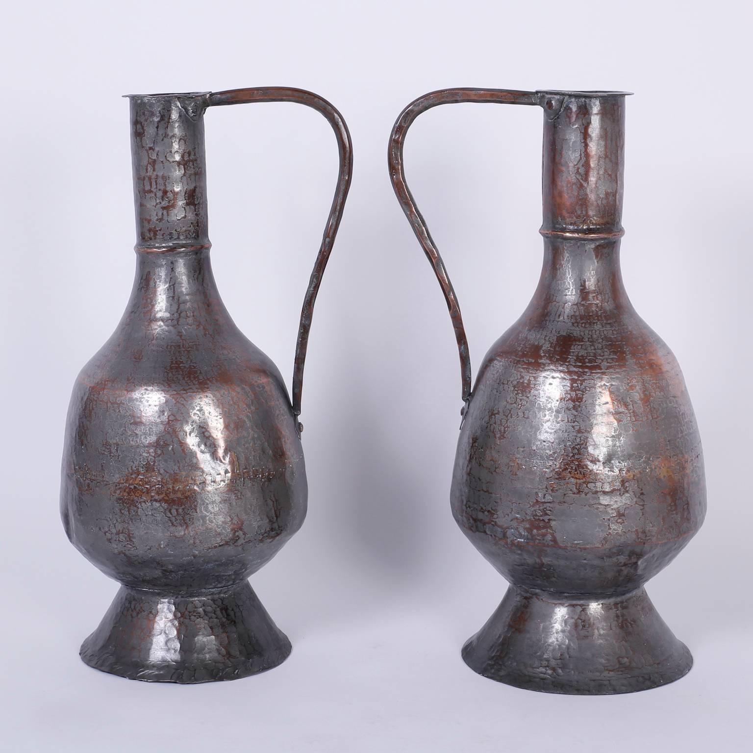 Antique pair of water pitchers or jugs handcrafted with copper, hammered, riveted, and plated with a translucent silver finish, giving them an acquired rustic quality only time and use can convey.