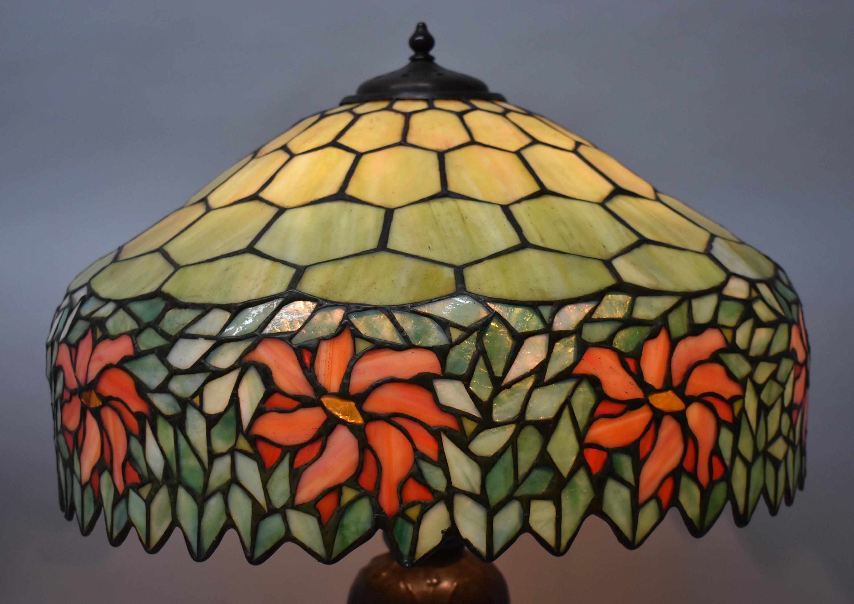 Antique Handel stained leaded glass table lamp with poinsettia details. Base has original patina with three Hubbell sockets and three acorn pulls. There is one small break in the small panes up around opening. Rewired with vintage style cloth cord.