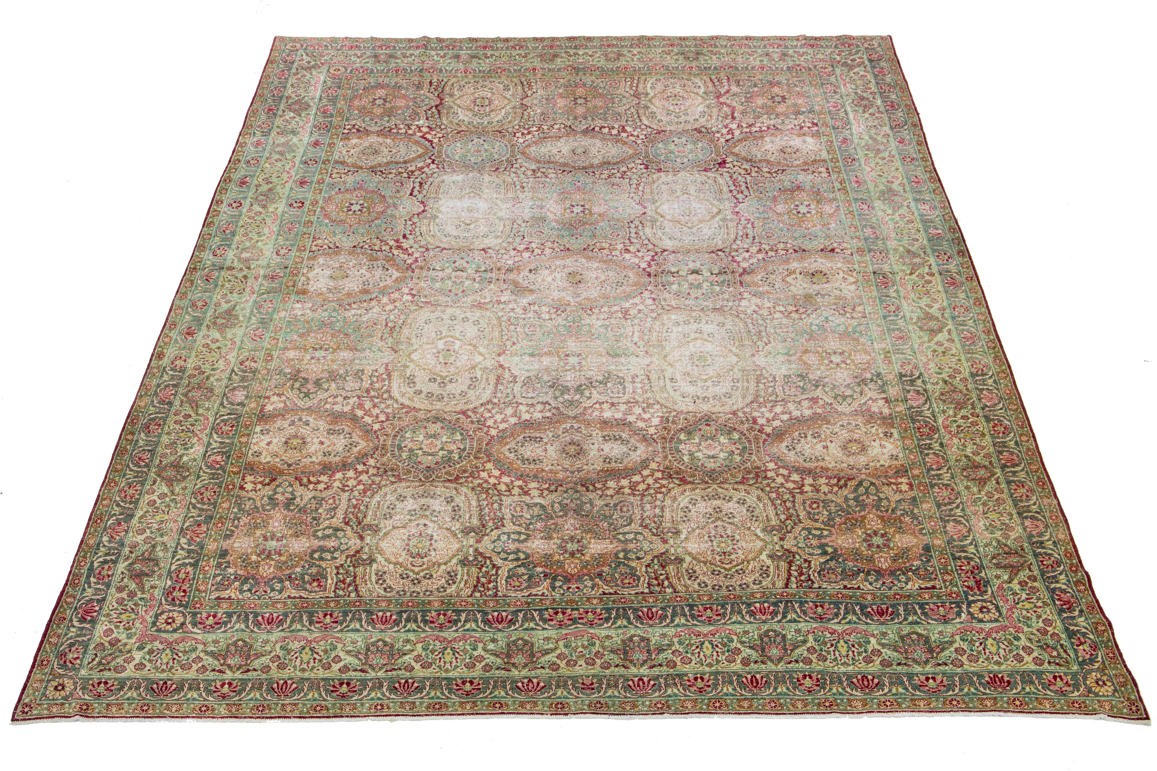 This hand-knotted wool rug from Kerman boasts a charming antique finish. The rug's raspberry-red color field is adorned with an all-over floral pattern, highlighted by hints of rich blue and rose—a remarkable piece of Persian craftsmanship.

This