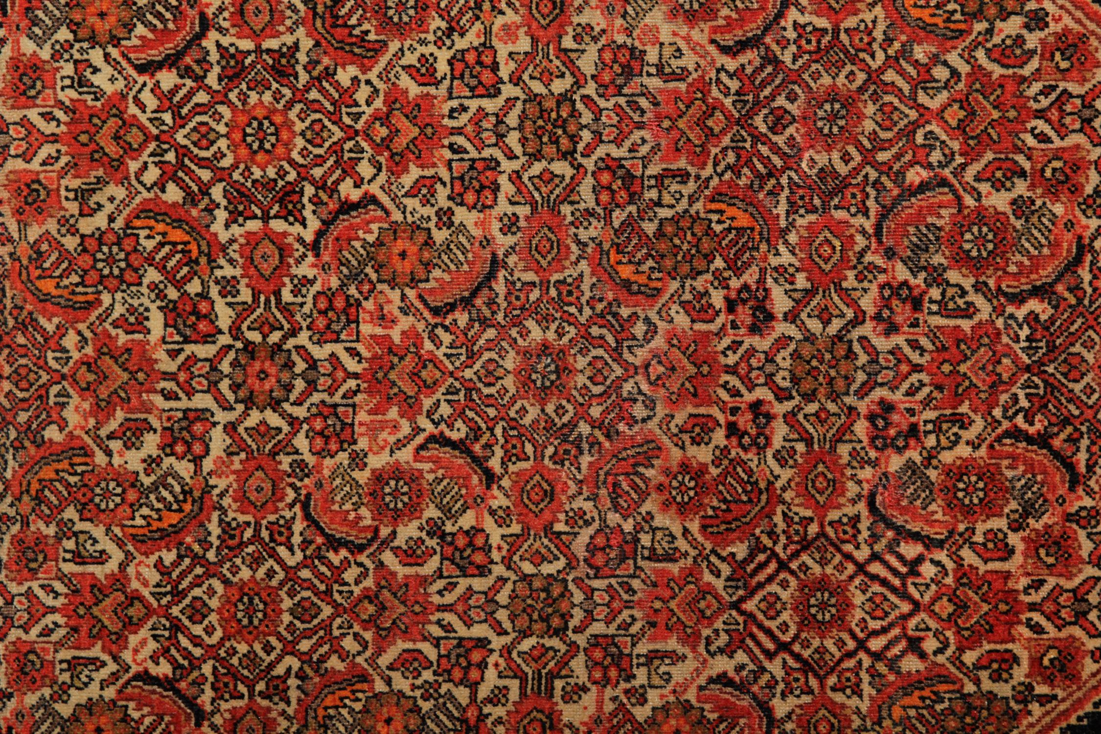 Dieser antike Teppich zeichnet sich durch ein einzigartiges All-Over-Muster aus, bei dem eine kühne schwarze Linie ein Trio von Diamanten in der Mitte umreißt. Der Hintergrund ist cremefarben mit orangefarbenen, braunen, rostfarbenen und roten