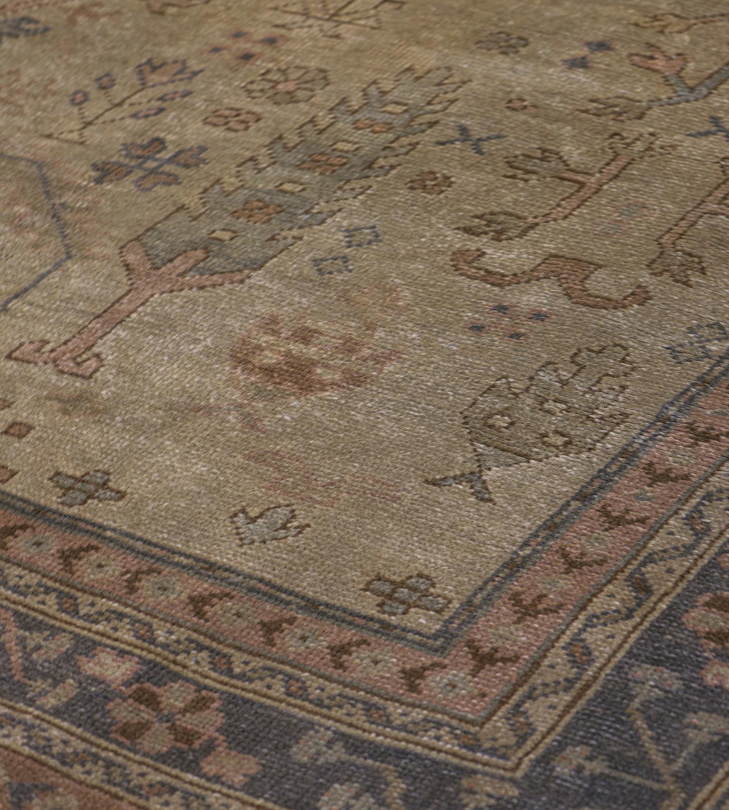 This antique Oushak rug features a shaded sandy-brown field with an overall design of angular trees issuing serrated arched leaves flanked by similar plants and flowerheads together with stylised floral vases, in a charcoal-grey border of angular