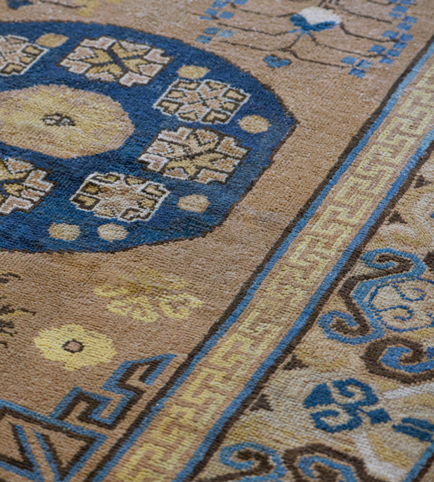 This traditional antique Persian Khotan runner has a sandy-brown field with various delicate floral sprays and hooked floral motifs around two shaded royal-blue roundels each containing a band of stellar angular flower head around a central panel,