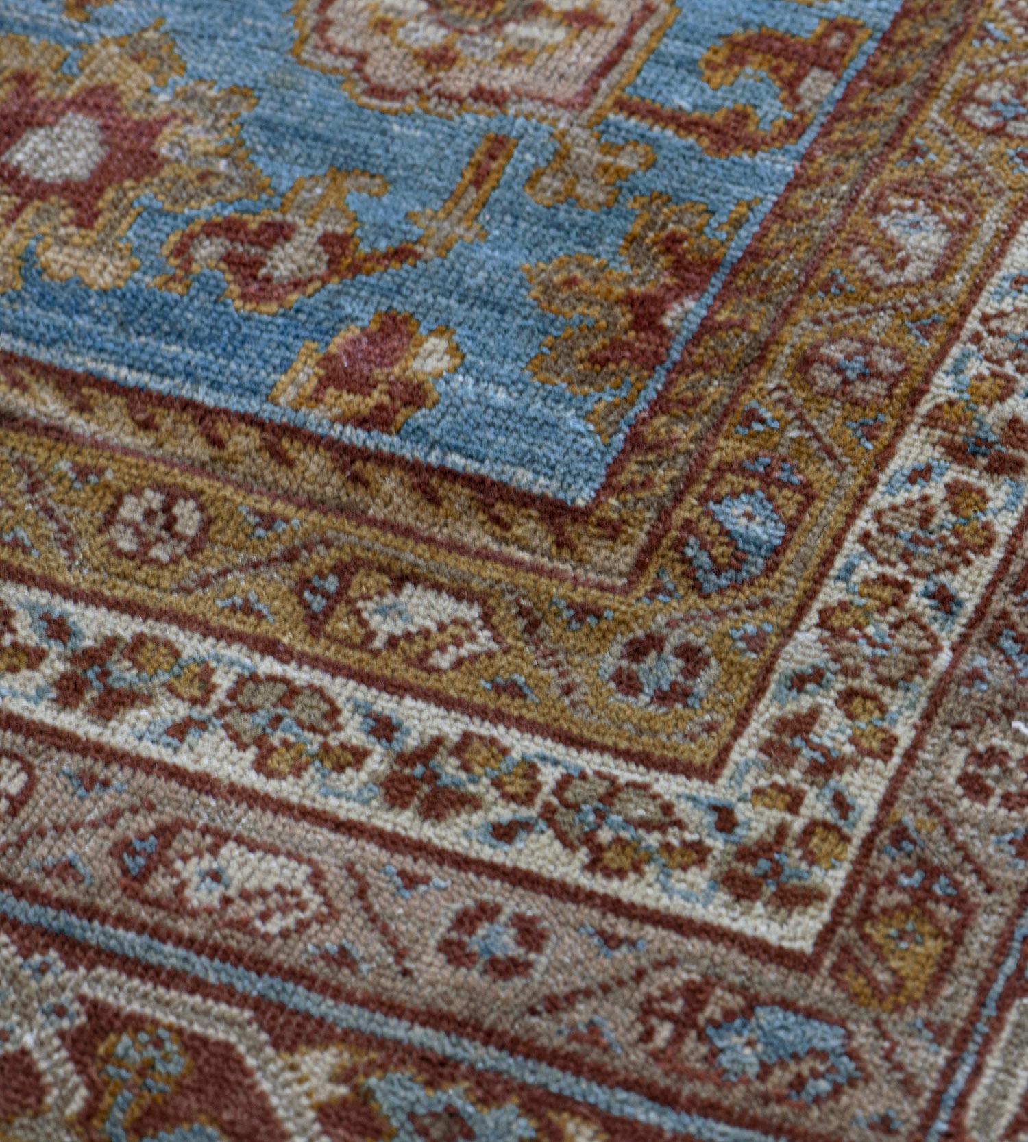 This traditional handwoven Persian Ziegler Sultanabad rug has a shaded medium-blue field with an overall design of angled taupe and rust palmettes enclosing central rosettes or lozenges issuing vines forming further lozenges, in a shaded rust border