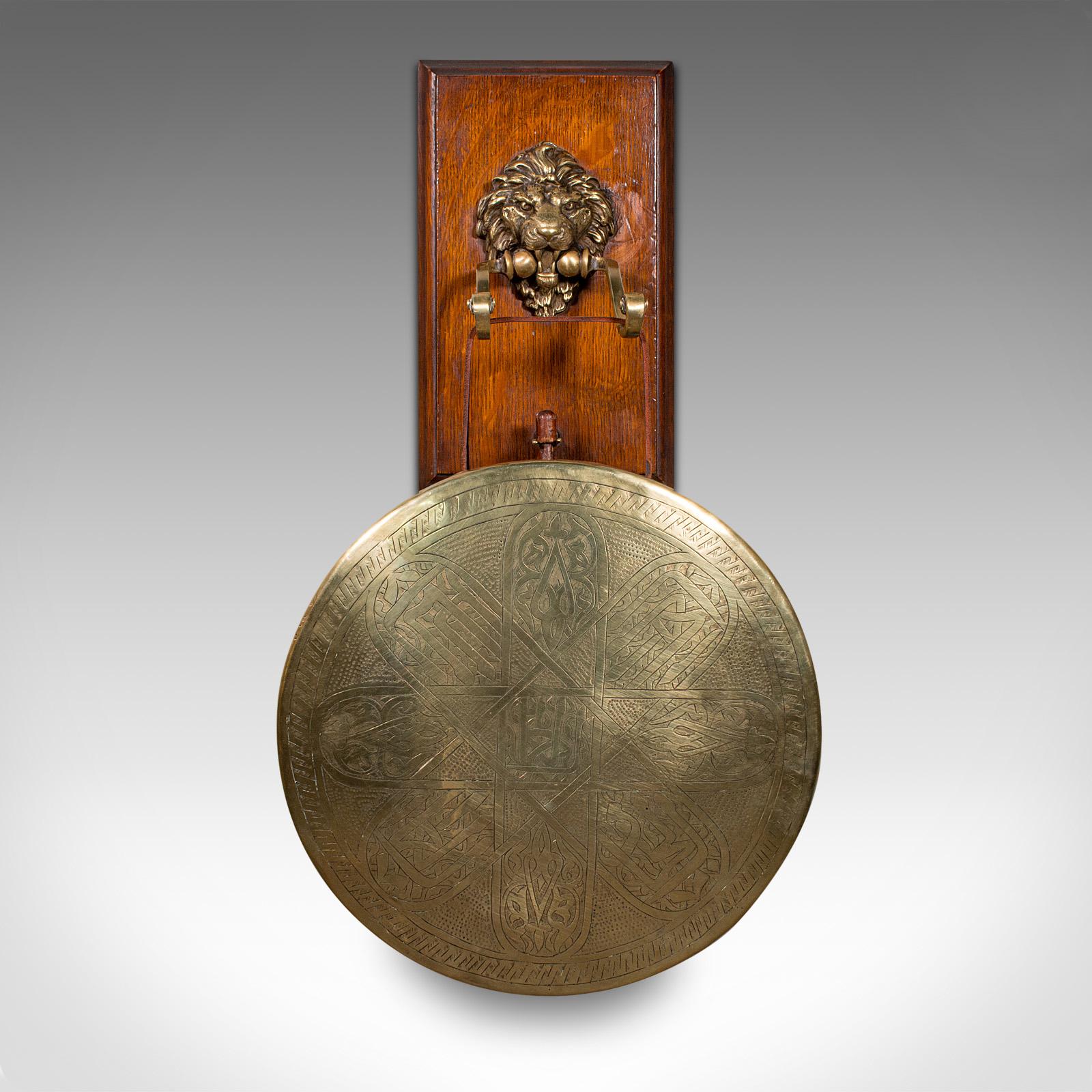 This is an antique hanging dinner gong. An English, brass and oak decorative mount, dating to the late Victorian period, circa 1880.

Of wonderful form and superb craftsmanship
Displays a desirable aged patina and in good order
Oak back rest