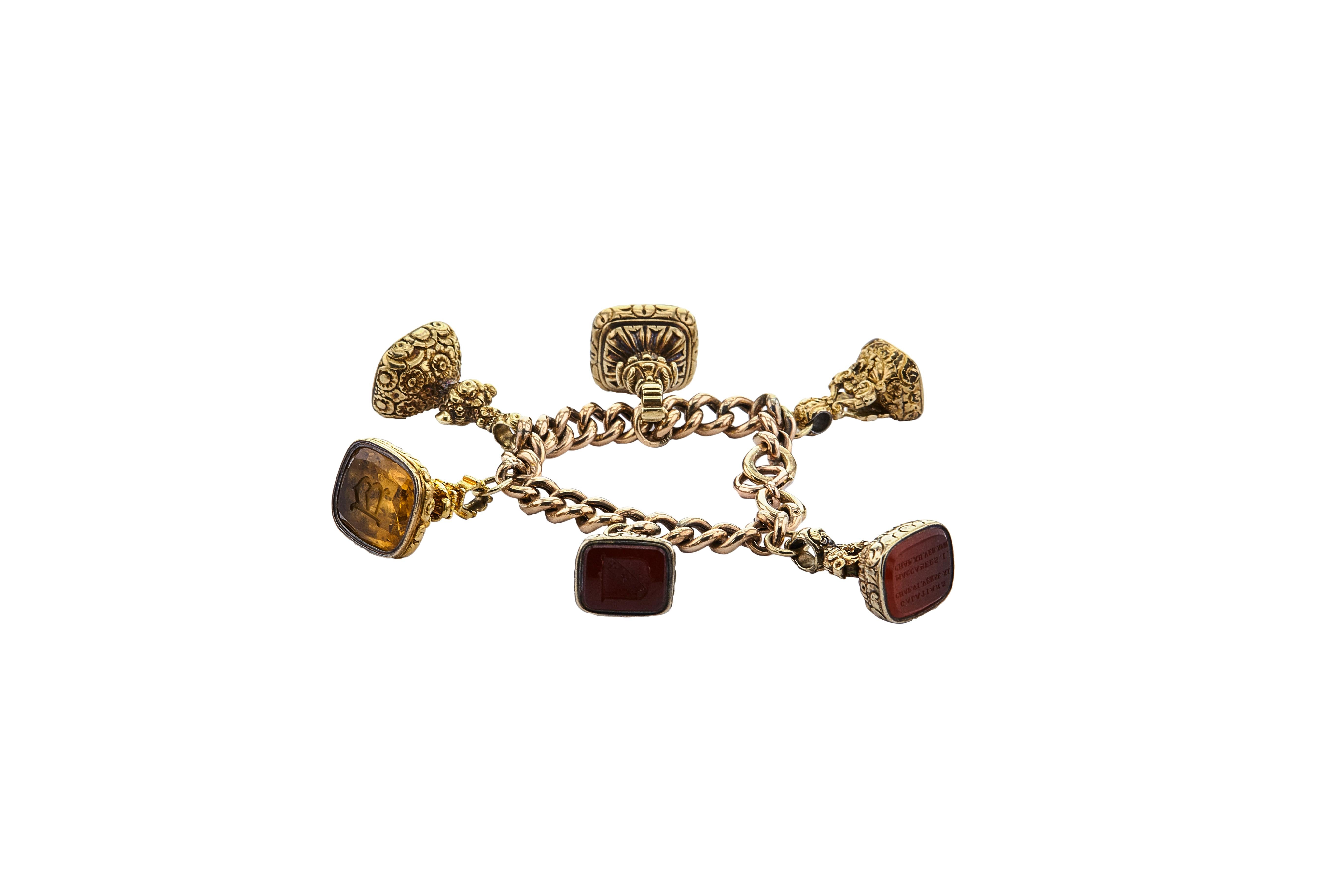 An antique charm bracelet comprising of six fancifully designed seals, each set with an intaglio engraving carved into various stones such as carnelian and quartz. The seals hang from an antique rounded curb bracelet measuring 7 inches. Crafted in 9