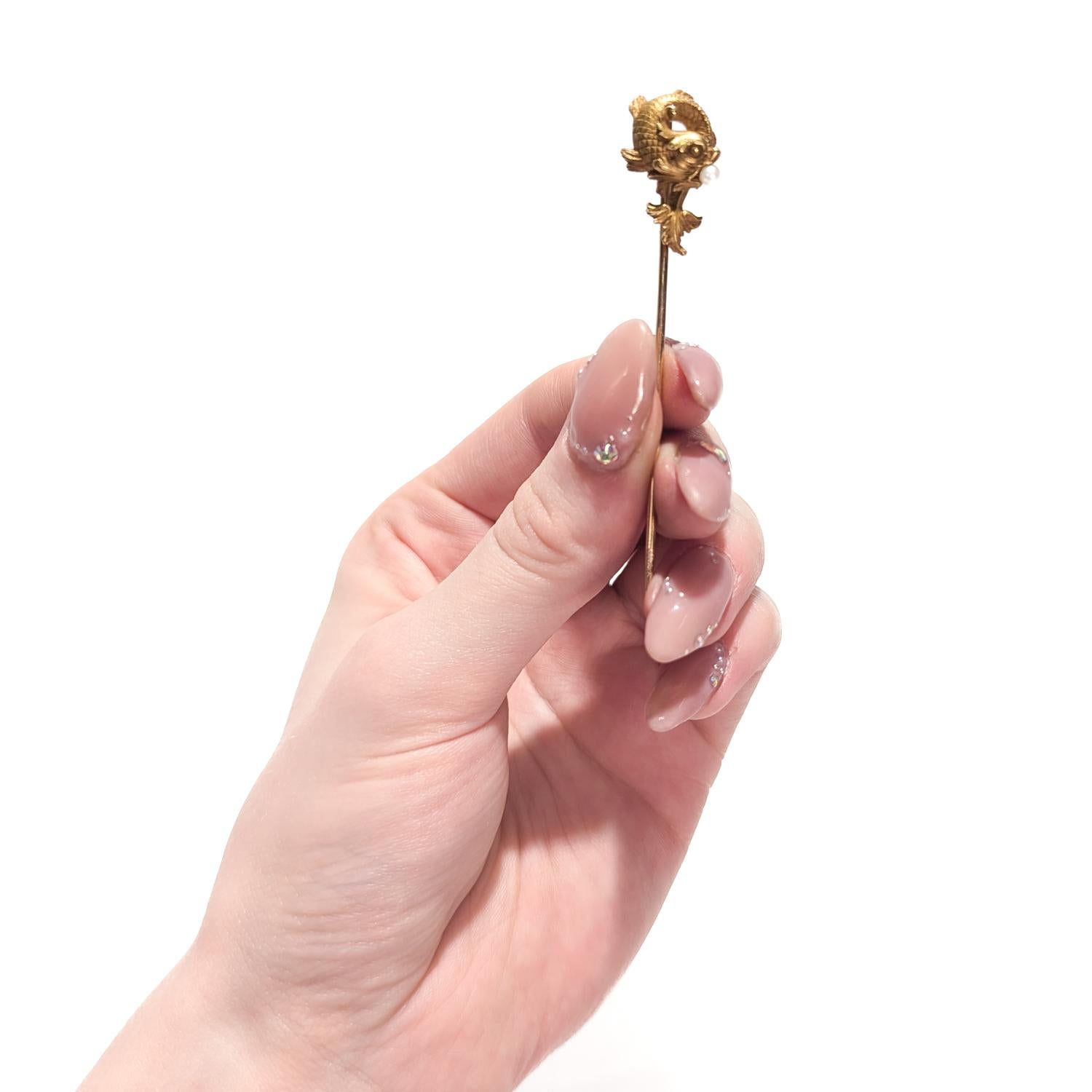 A signed antique French stickpin.

In 18 karat yellow gold. 

By Hartz et Cie.

In a Renaissance Revival style.

The head in the form of a stylized dolphin or carp holding a pearl in its mouth.

Later in his career, Hartz joined forces with Edmond