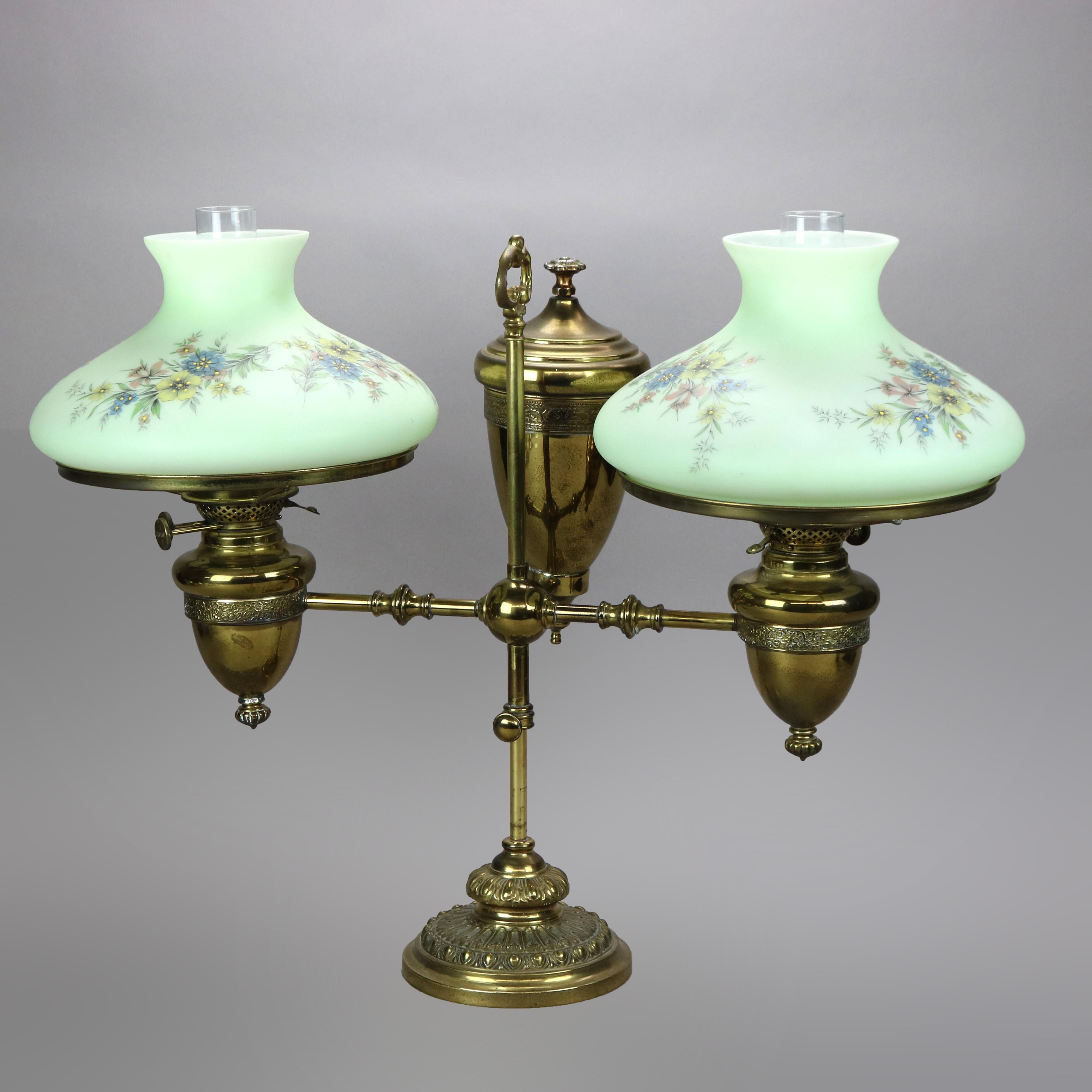 An antique Harvard school double student oil lamp by Duplex offers brass frame with adjustable arm terminating in two lights having hand painted floral cased glass shades, raised on base having embossed floral elements, not electrified,