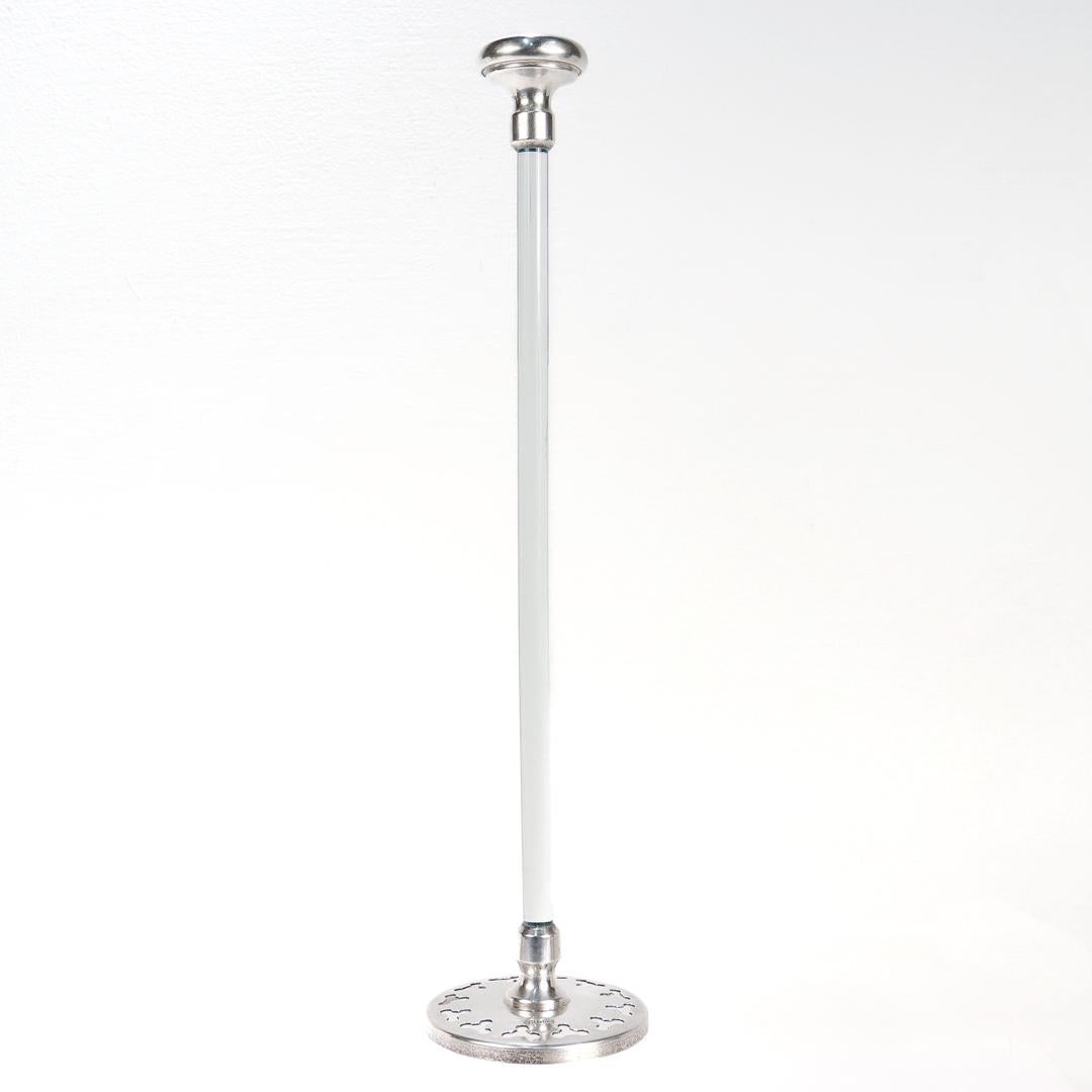 A fine antique cocktail strainer or plunger shaped mixer.

In sterling silver and glass. 

By Hawkes.

Consisting a rounded silver handle connected by a cylindrical glass rod to a wide flat silver plunger with small holes in it.

Marked Sterling to
