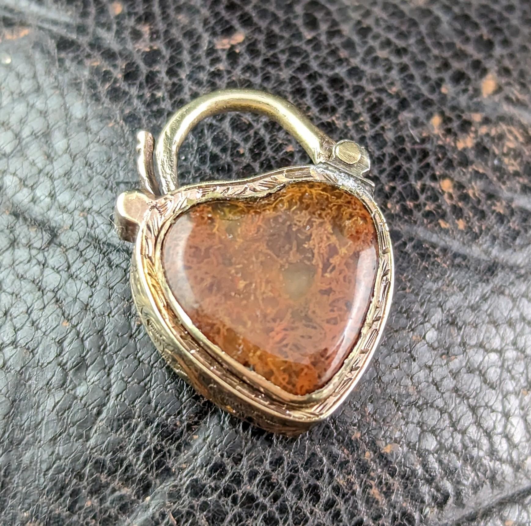 This is just the sweetest little antique 9kt gold heart shaped padlock, locket pendant. 

Victorian era it has an elaborately engraved body with one side set a brown mossy agate heart and the other side featuring a glazed locket compartment