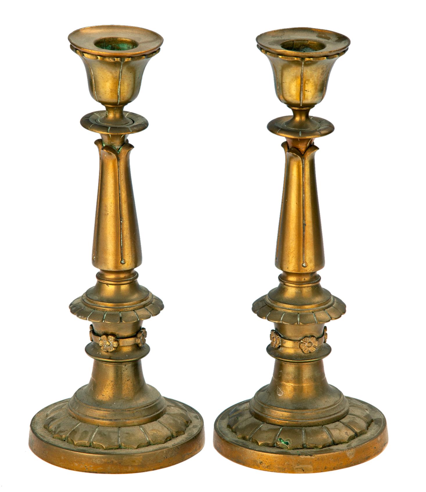 This pair of beautiful brass candlesticks have classical simplicity.
Exquisitely crafted in the distinct style of the 1st empire period in France. 
Quite heavy with a smooth patina, 
Adorned with decorative motifs & banded with small, linked flowers.