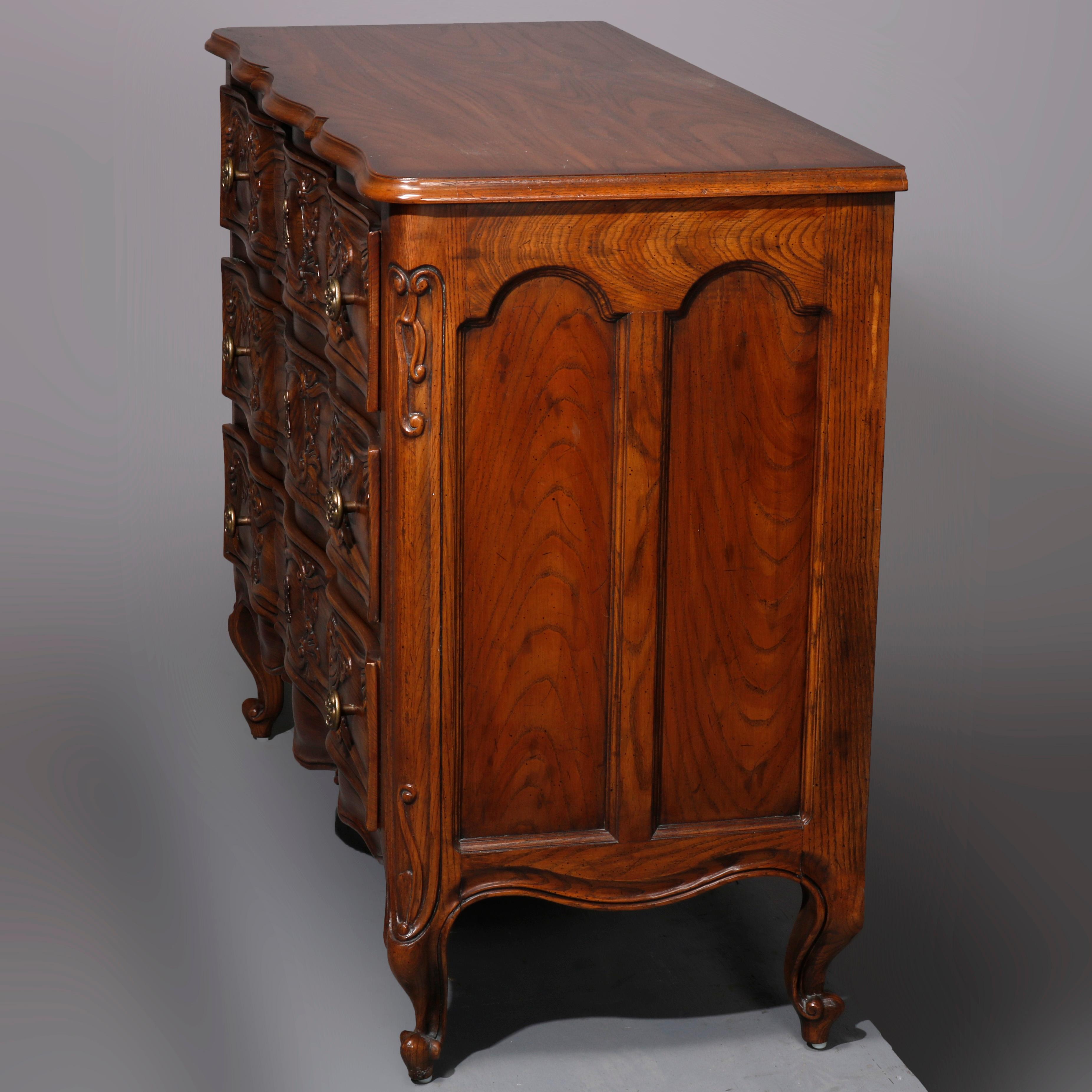 An antique French Louis IV style chest of drawers by Henredon offers oak construction with shaped top surmounting swell front chest with three shaped drawers having carved foliate elements, paneled sides, raised on cabriole legs terminating in