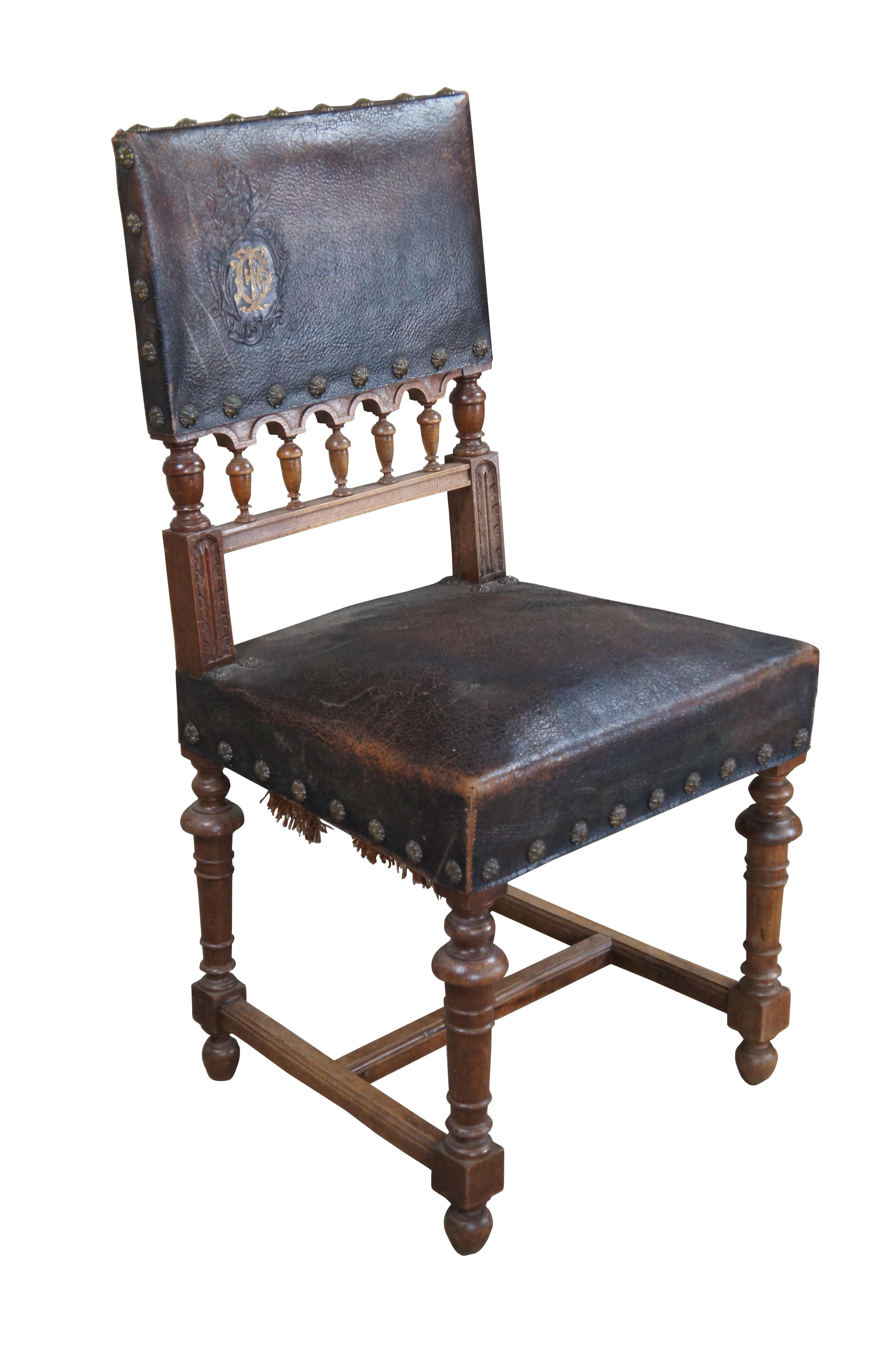 Antique Henry II style dining side chair, circa 1880s. Made from walnut with an embossed leather back featuring a crest and winged griffon. The lower back of the chair showcases an carved arvade with turned finials. Chair stiles have a carved