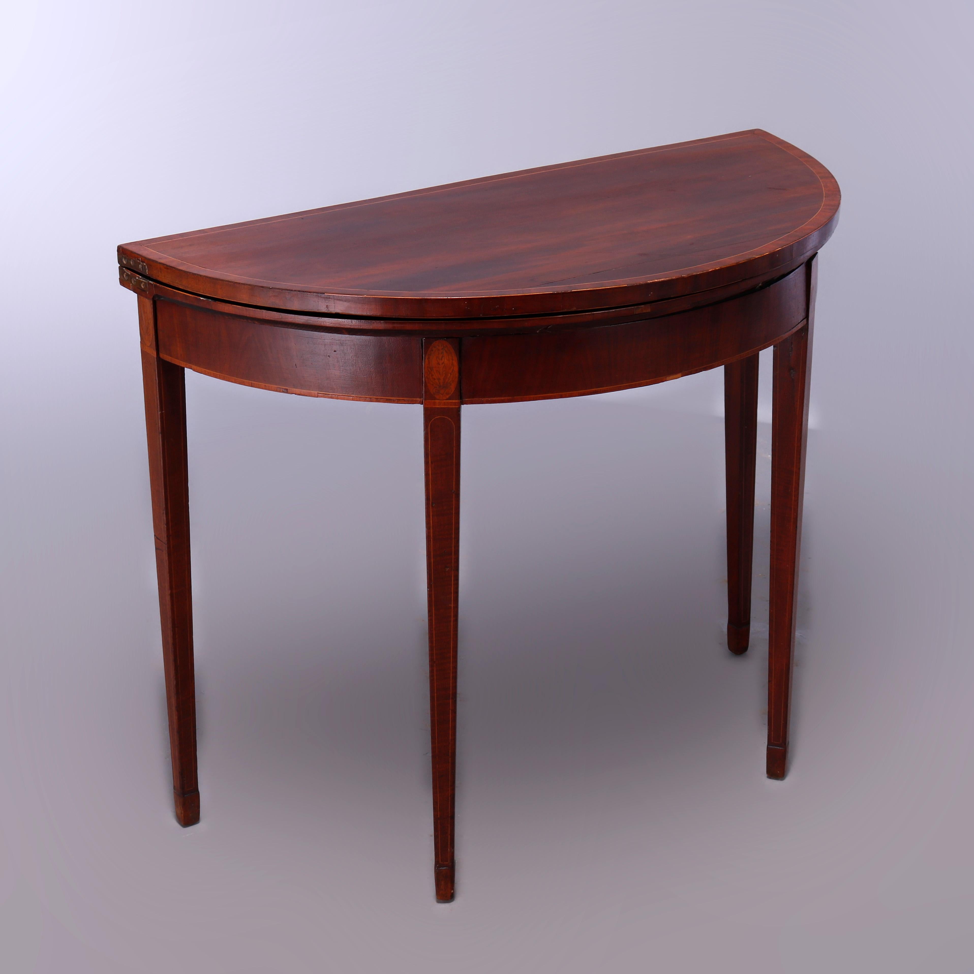 An antique Hepplewhite game table offers Mahogany construction in demilune form with satinwood banding with top opening to sunburst playing surface and raised on tapered square legs having inlaid medallions at the capitals, c1820

Measures-