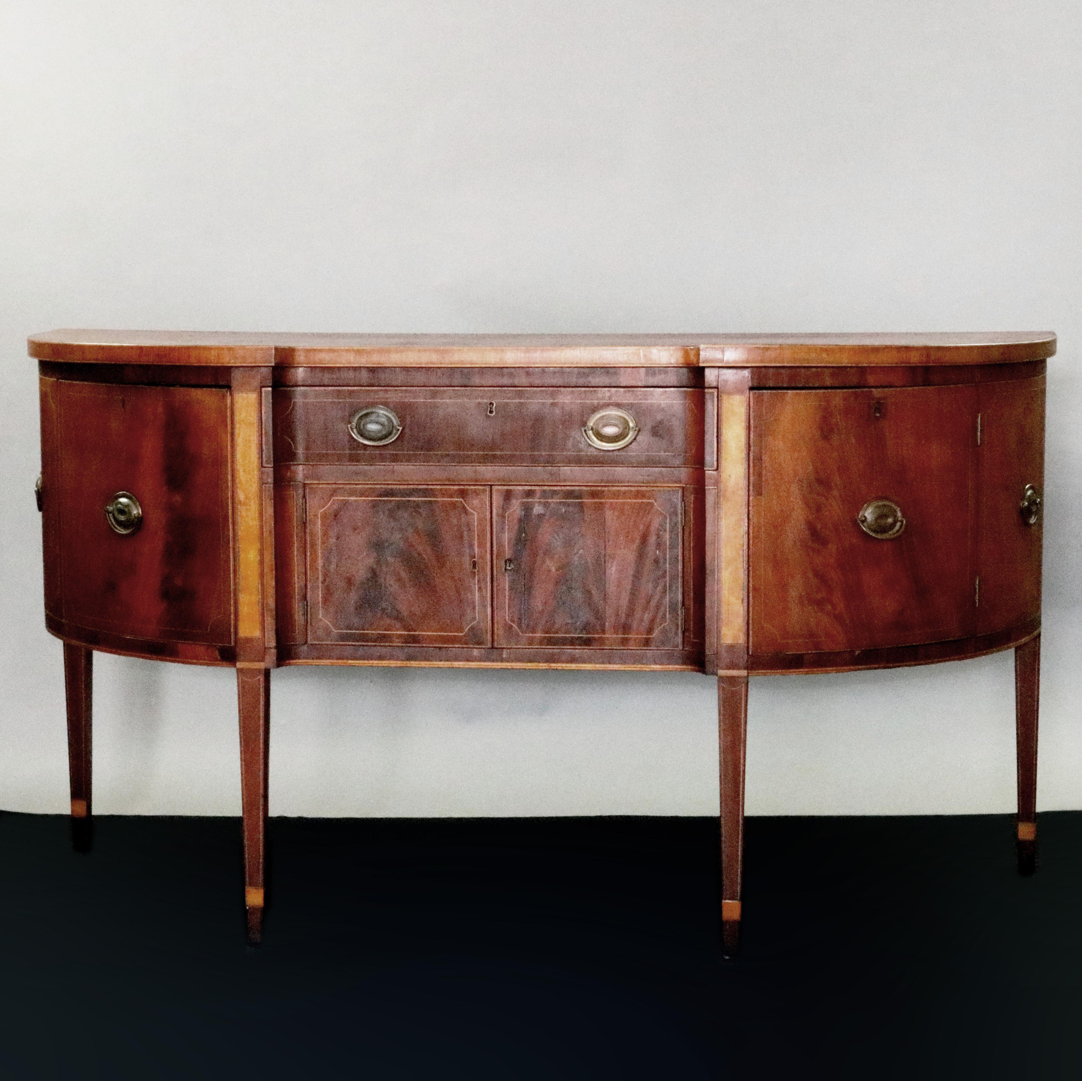 An antique Hepplewhite sideboard offers flame mahogany construction in demilune form with central frieze drawer over lower double door cabinet with flanking side cabinets and having satinwood inlay banding throughout, raised on square, straight and