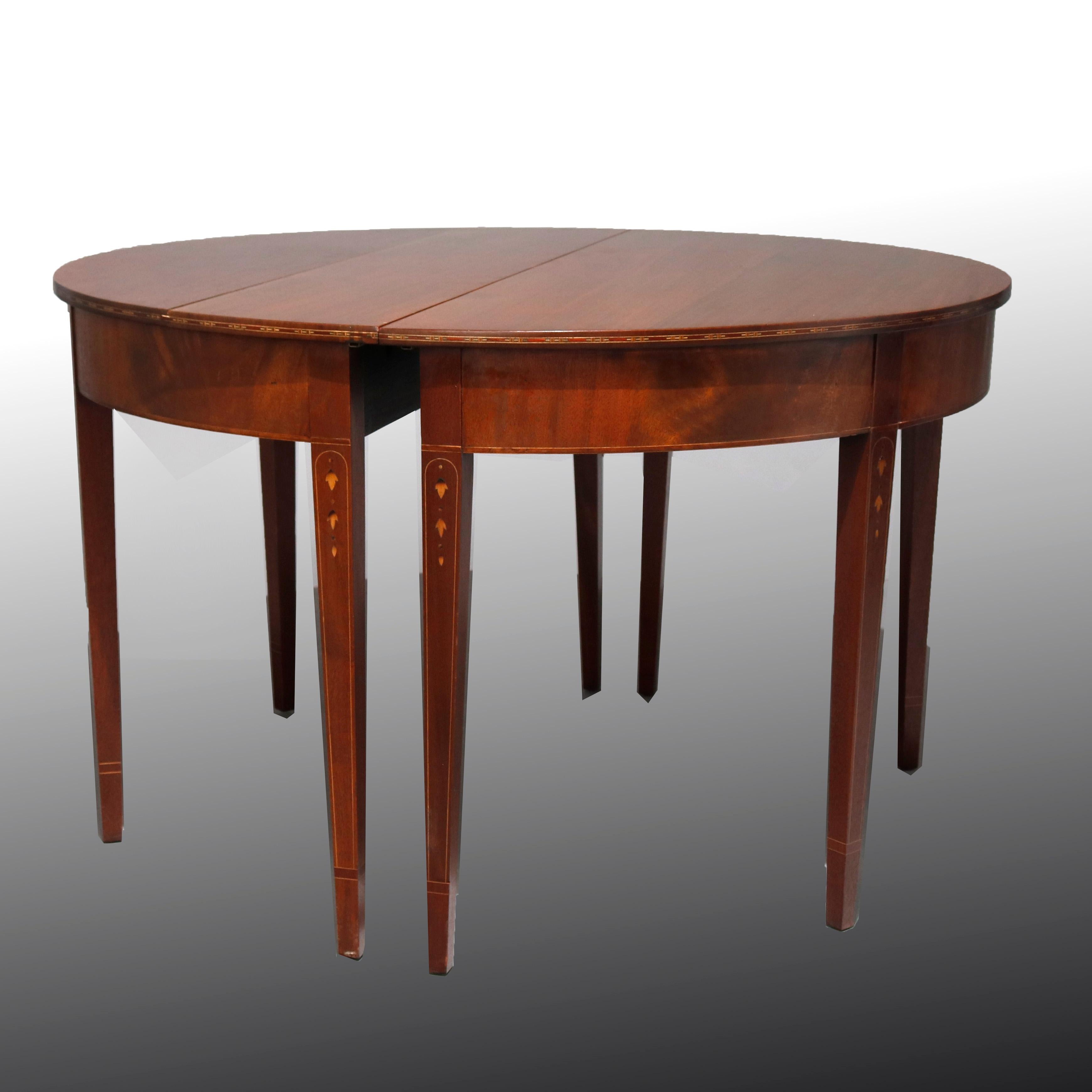 An antique English Hepplewhite style banquet table offers flame mahogany construction with top having deep skirt and raised on square and tapered legs with inlaid satinwood banding and inverted bellflowers, includes two demilune ends with central