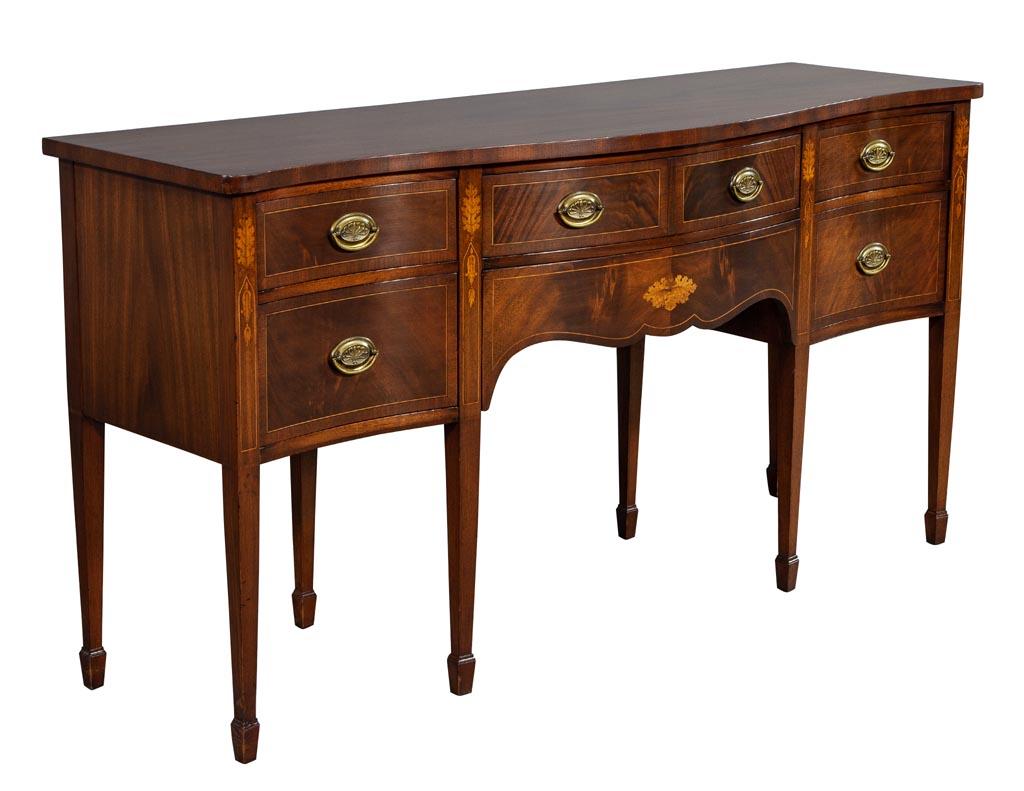 Antique Hepplewhite style mahogany sideboard buffet. Vintage American made Hepplewhite style sideboard in original excellent condition. The piece is inlaid with marquetry mahogany and still adorned with its original oval brass handles. A timeless