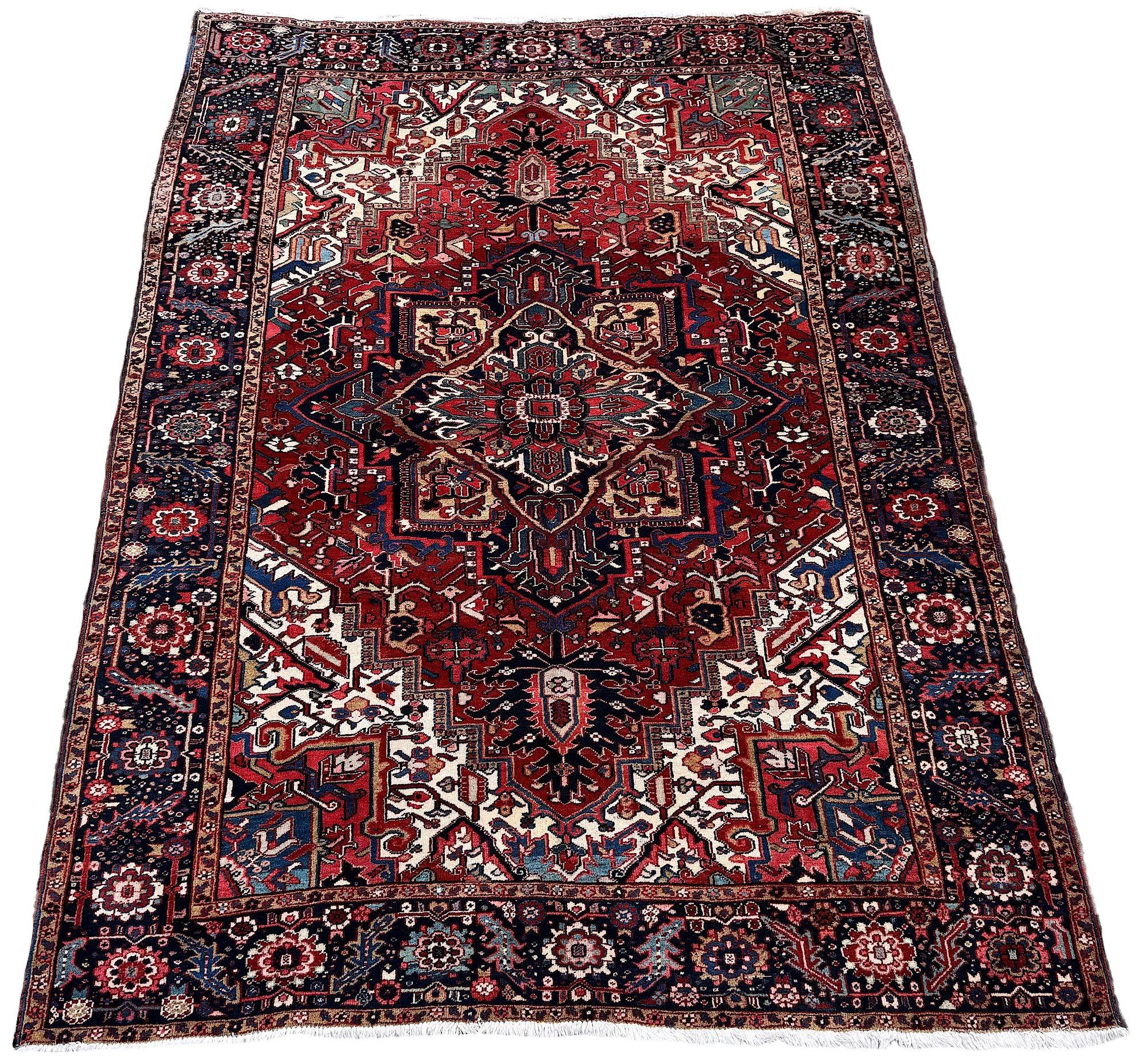 A beautiful antique Heriz carpet, woven circa 1920. The design features a large geometrical medallion on a rich terracotta field surrounded by a classic deep blue border. Very attractive secondary colours of pinks, greens and golds and a highly