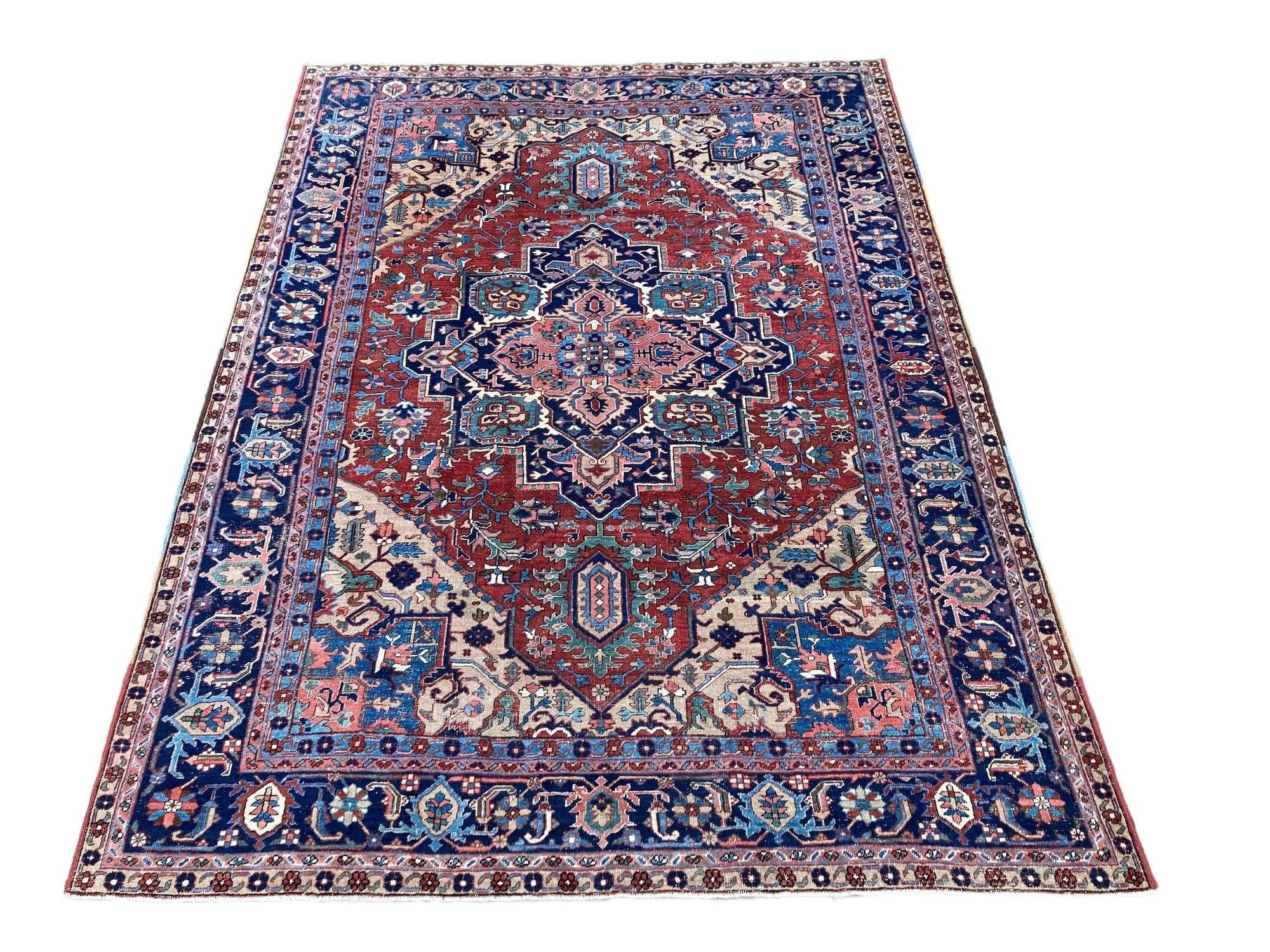 A fabulous antique Heriz carpet, hand woven circa 1900 with a large geometrical medallion on a terracotta field and deep indigo border. Fabulous secondary colours of blues, greens and salmon pink and a highly decorative piece. Size: 3.43m x 2.56m