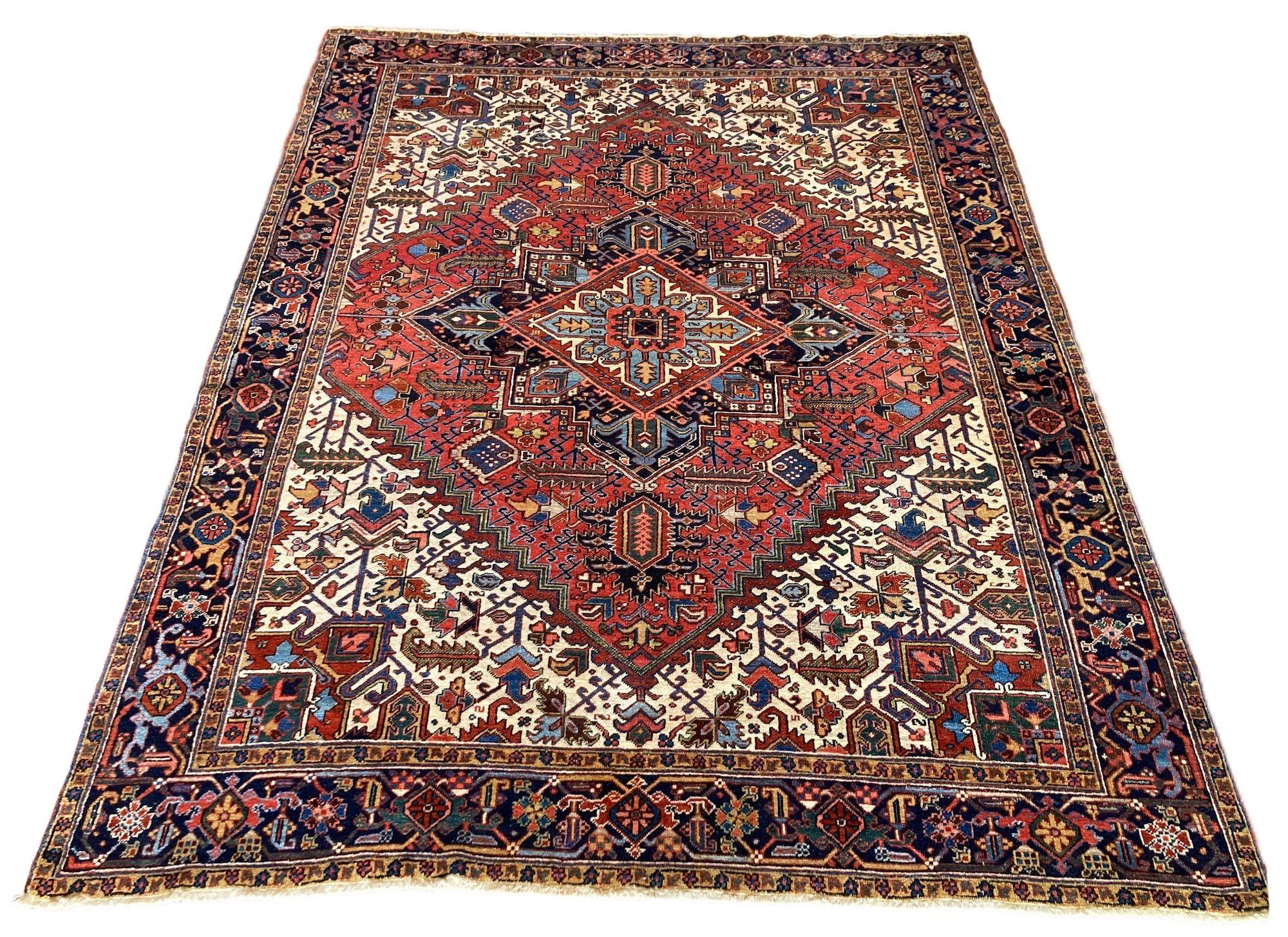 Ein schöner antiker Heriz-Teppich, handgewebt um 1910 mit einem traditionellen geometrischen Muster auf einem Terrakotta-Feld und einer tiefen indigoblauen Bordüre. Ein besonders ausgewogenes Design mit großen elfenbeinfarbenen Eckzwickeln und