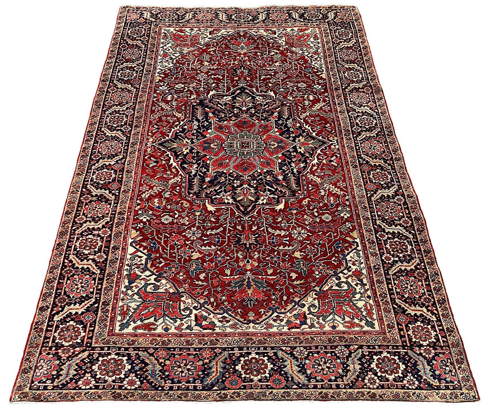 A wonderful antique Heriz carpet, hand woven circa 1920. The design features a large, geometrical central medallion surrounded by stylised flowers and vines on a rich terracotta field and particularly attractive indigo border. A very decorative