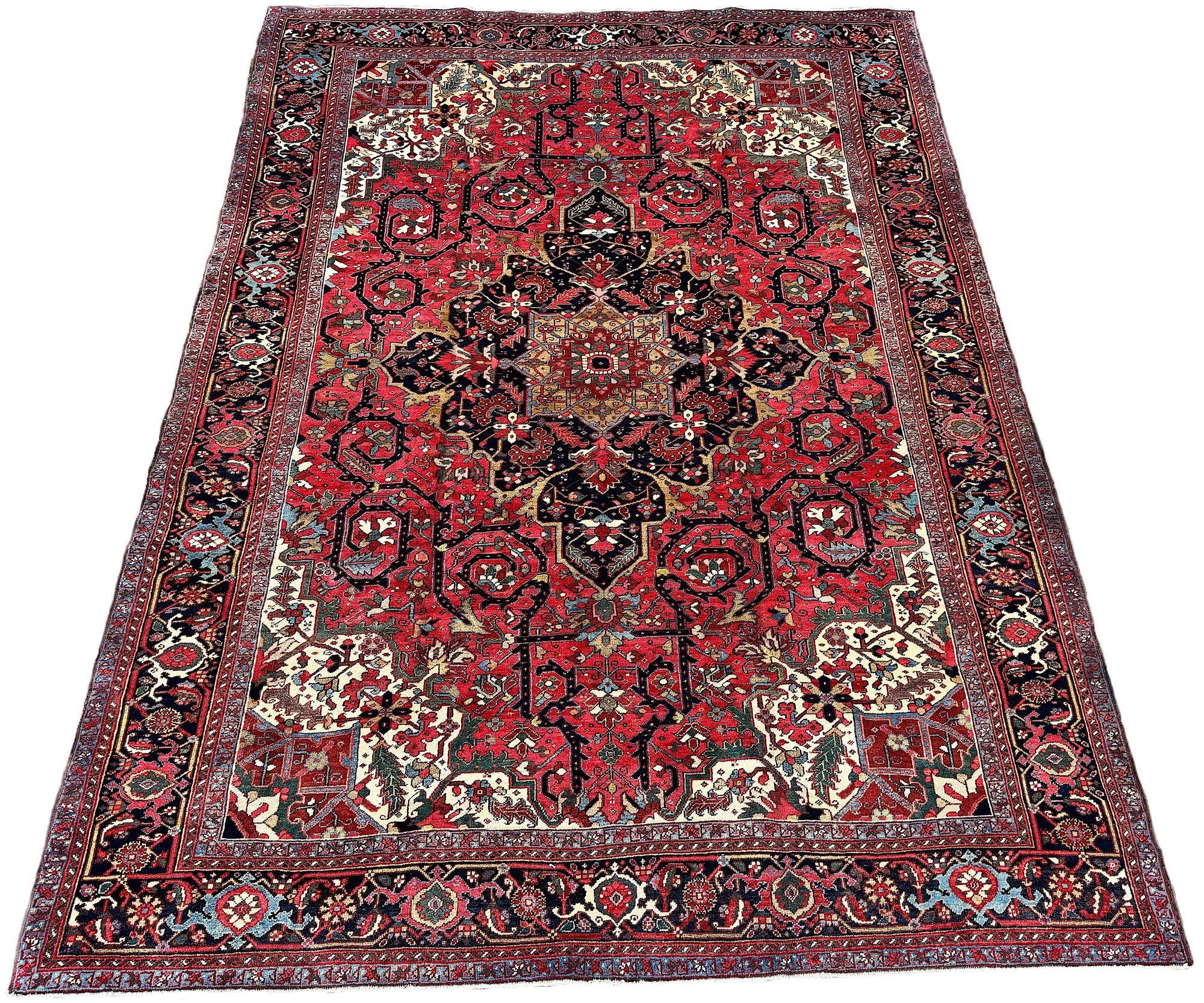 An exceptional antique Heriz carpet, woven circa 1920. The design features a large geometrical medallion on a rich terracotta field surrounded by a classic deep blue border. The design is very unusual with the scrolling vines in the field and the