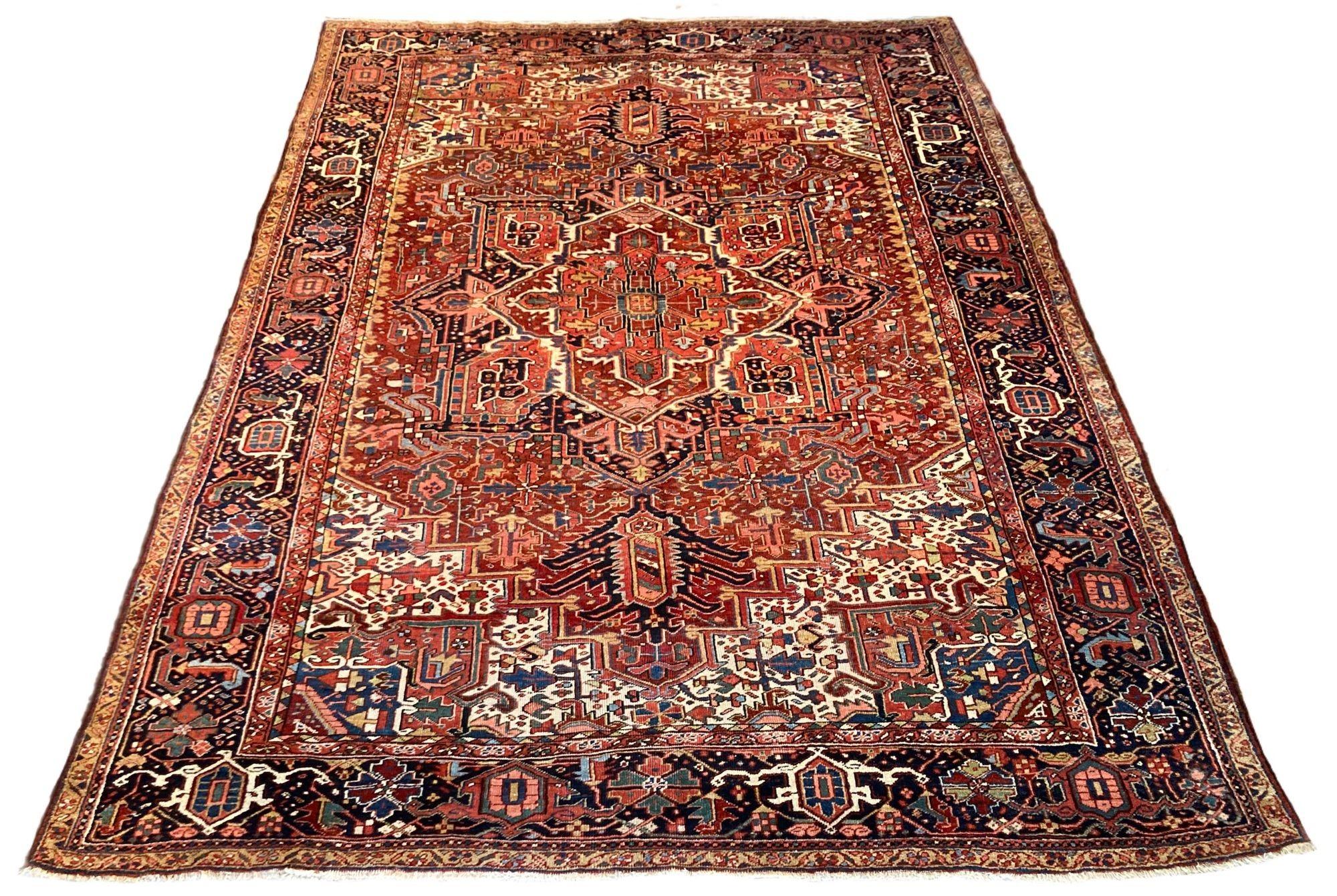 A wonderful antique Heriz carpet, hand woven circa 1920. The design features a large, geometrical central medallion surrounded by stylised flowers and vines on a rich terracotta field. Some interesting design elements include the innermost border of
