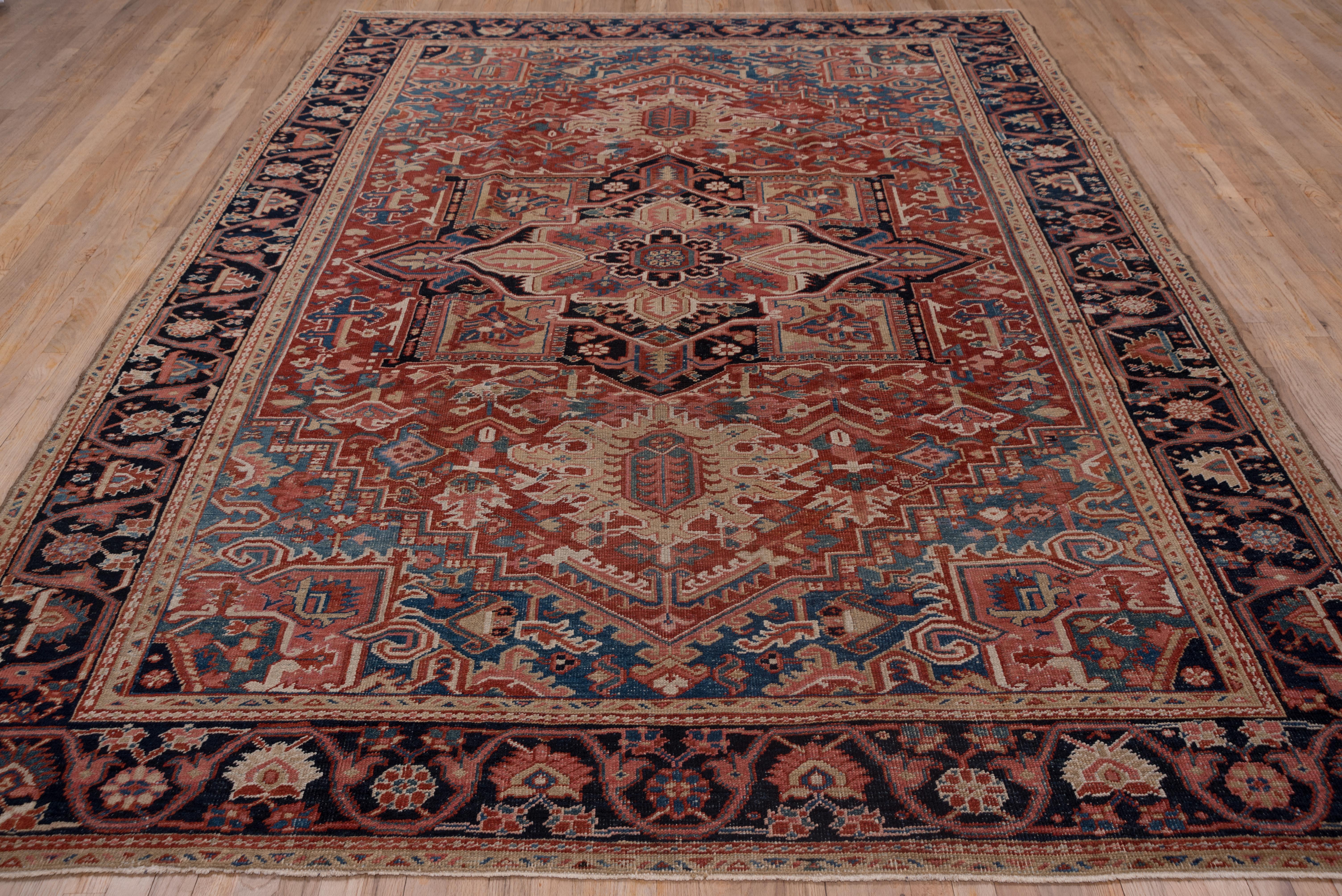 This classic NW Persian rural carpet displays a tomato red subfield, navy pendanted octogramme medallion and sky blue corners extending into the sides as an encompassing field. The colors are mellow with age and the bottle green, salmon-buff and