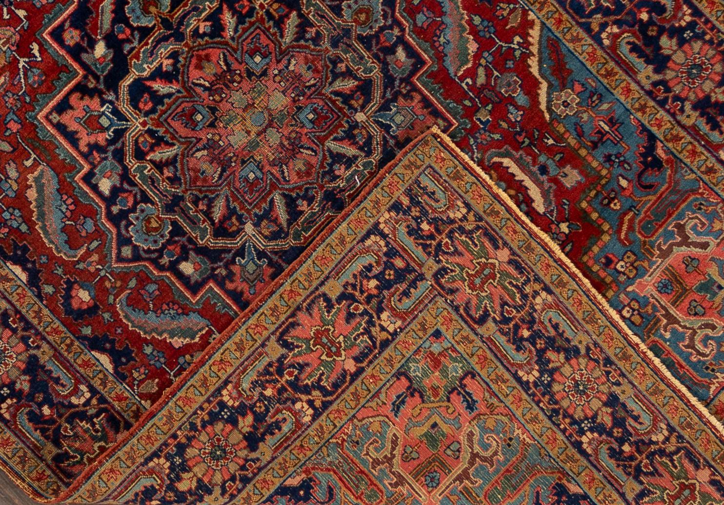 An early 20th century antique Heriz rug with a center medallion in an all over red and blue geometric motif and a border. This rug measures at 6'5