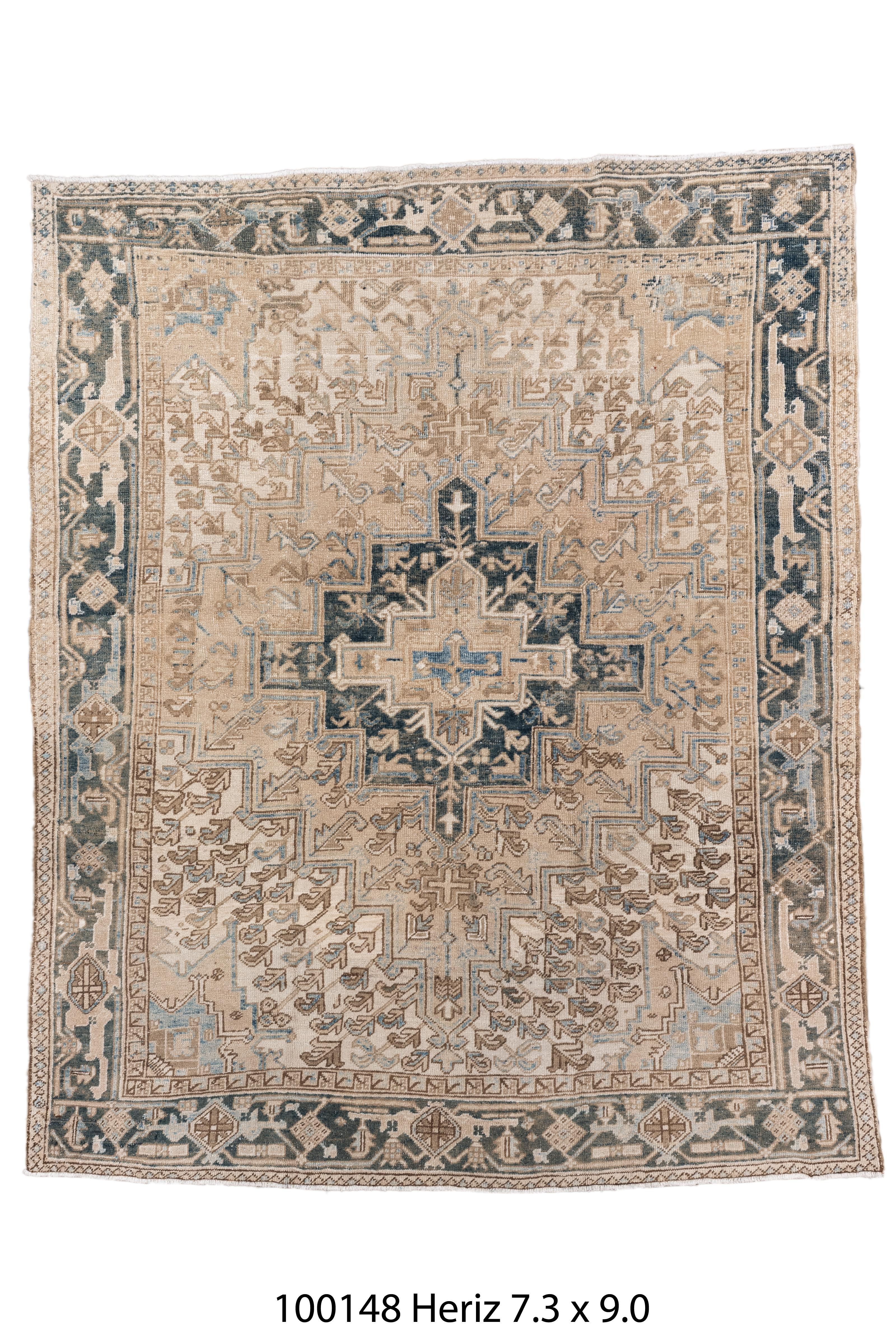 A sophisticated antique Heriz rug, hand-knotted in Northwest Persia, showcasing a striking geometric medallion design with a soft, washed palette of dusty taupe, pale camel, muted indigo, and ivory. The bold central motif, outlined in rich denim and