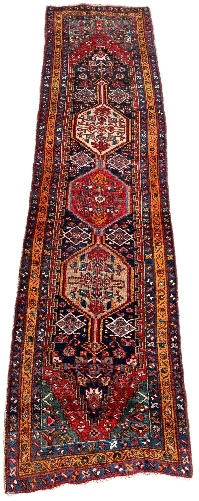 A charming antique Heriz runner, woven circa 1920. The design features a three geometrical medallions on a deep indigo field surrounded by a tangerine border. Vibrant secondary colours of reds, pinks and greens and a very cheerful runner. Slightly