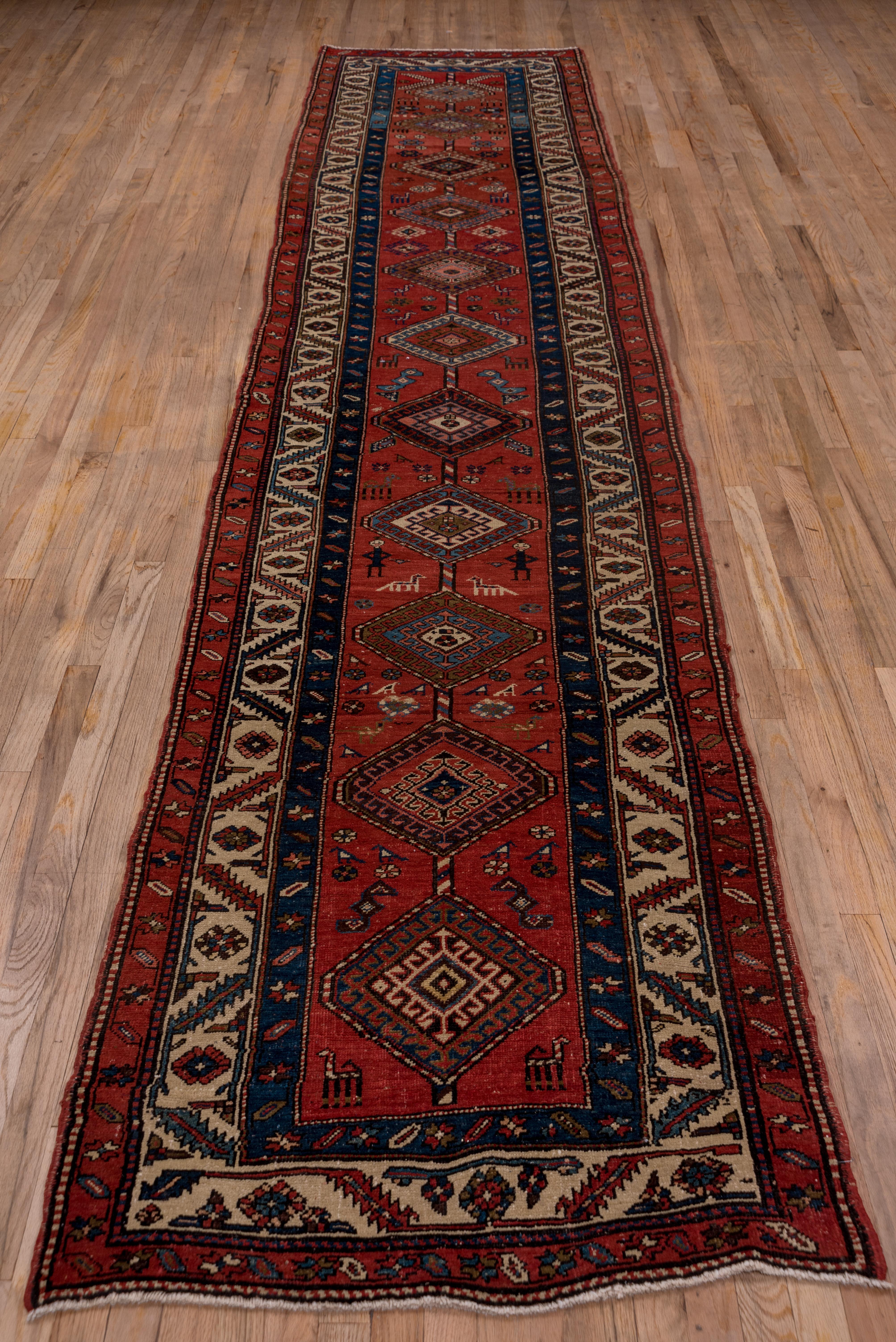 This very good condition NW Persian village runner displays a central pole medallion of 11 internally hooked hexagons flanked by birds, animals, human figures and rosettes on a ruby red field. The main ivory border displays the classic slanted,
