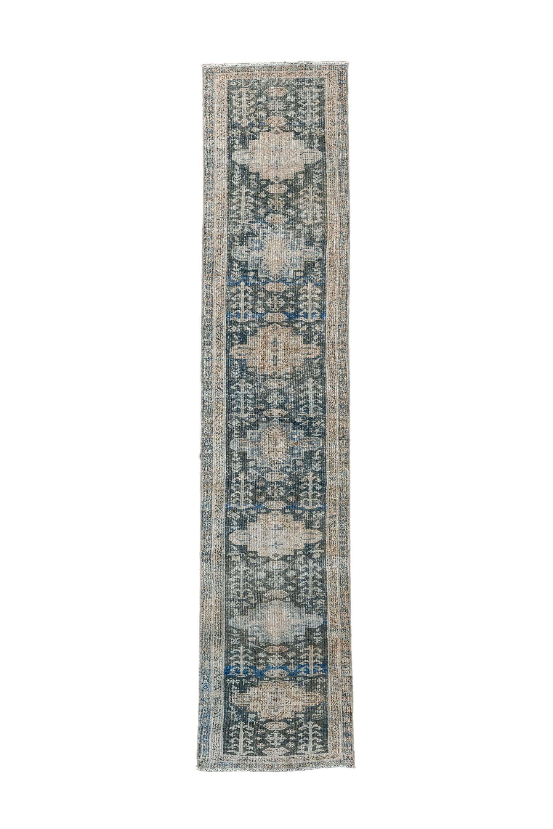 The blue field features  seven similar cartouches in green and straw, with herringbone plants alongside along with tiny tertiary flowers and birds. Ivory inner border. Moderate weave. Unusually narrow for the length.

Rug Size
2'4x10'10