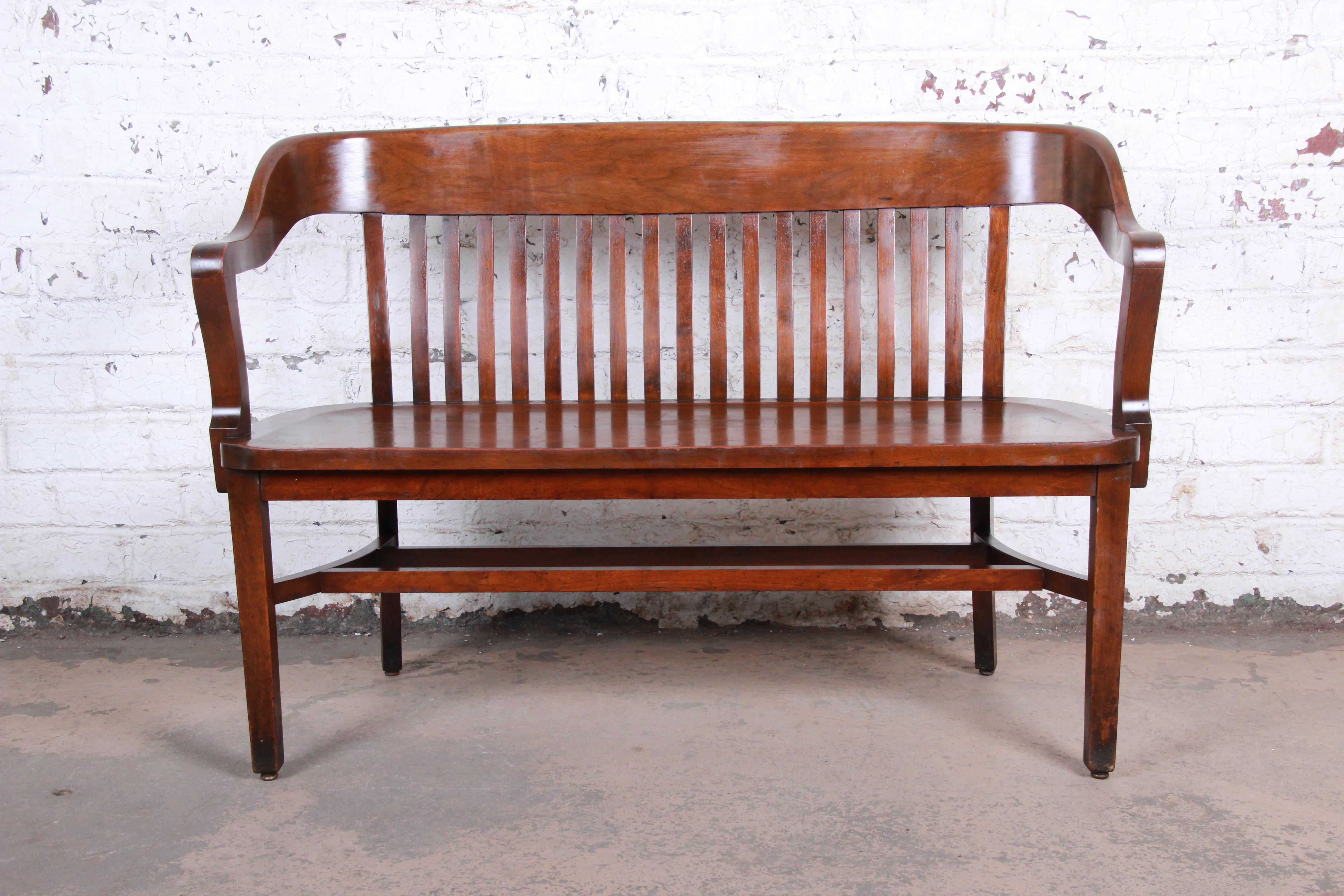 A gorgeous antique lawyer's bench by Heywood-Wakefield. The bench is made from solid walnut and is both sturdy and comfortable. A beautiful statement piece for an entryway or office. The original Heywood-Wakefield tag is present on the bottom of the