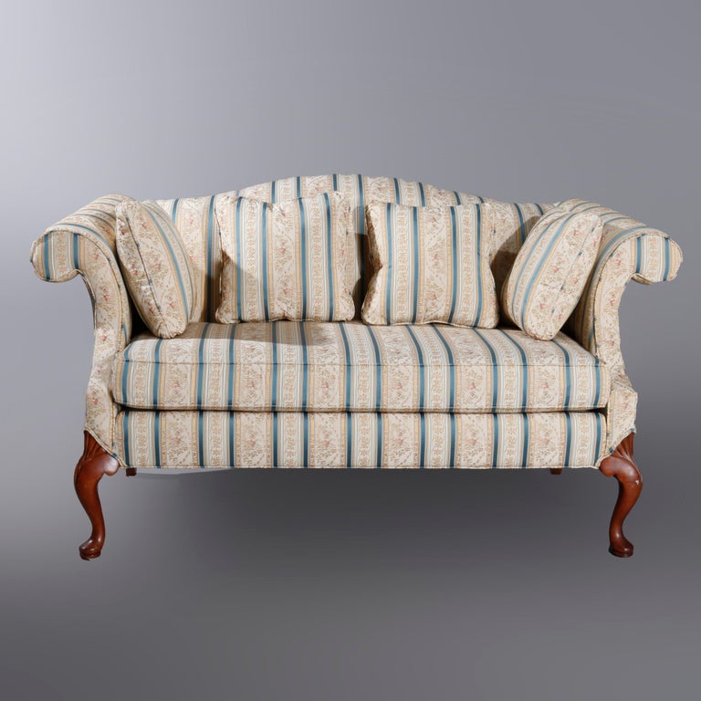 An antique Queen Anne style settee by Laine of Hickory offers camel back form with scroll arms, raised on mahogany cabriole legs with stylized carved shell and scroll knees and pad feet, fully upholstered, maker label as photographed, 20th