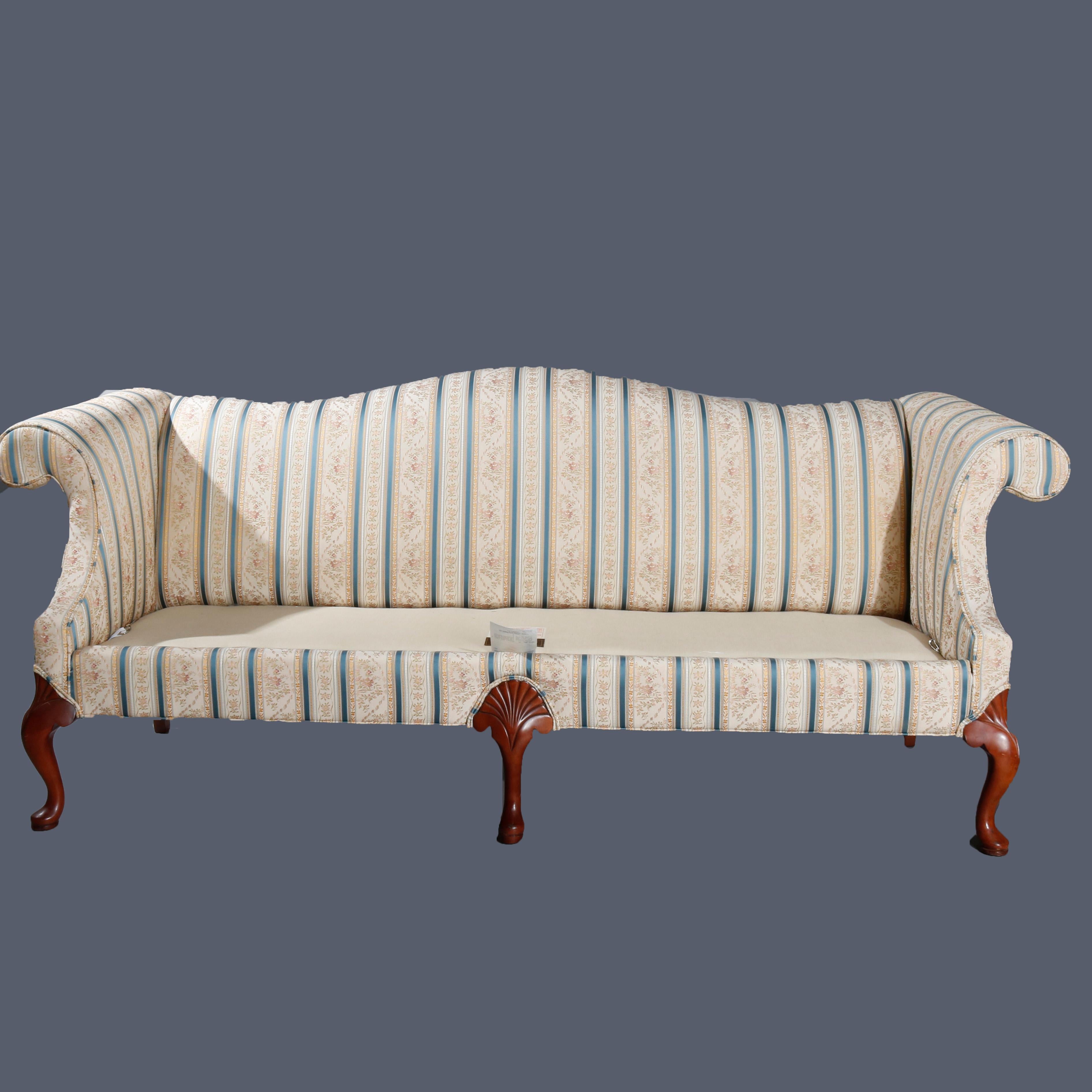 An antique Queen Anne style sofa by Laine of Hickory  offers camel back form with scroll arms, raised on mahogany cabriole legs with stylized carved shell and scroll knees and pad feet, fully upholstered, maker label as photographed, 20th