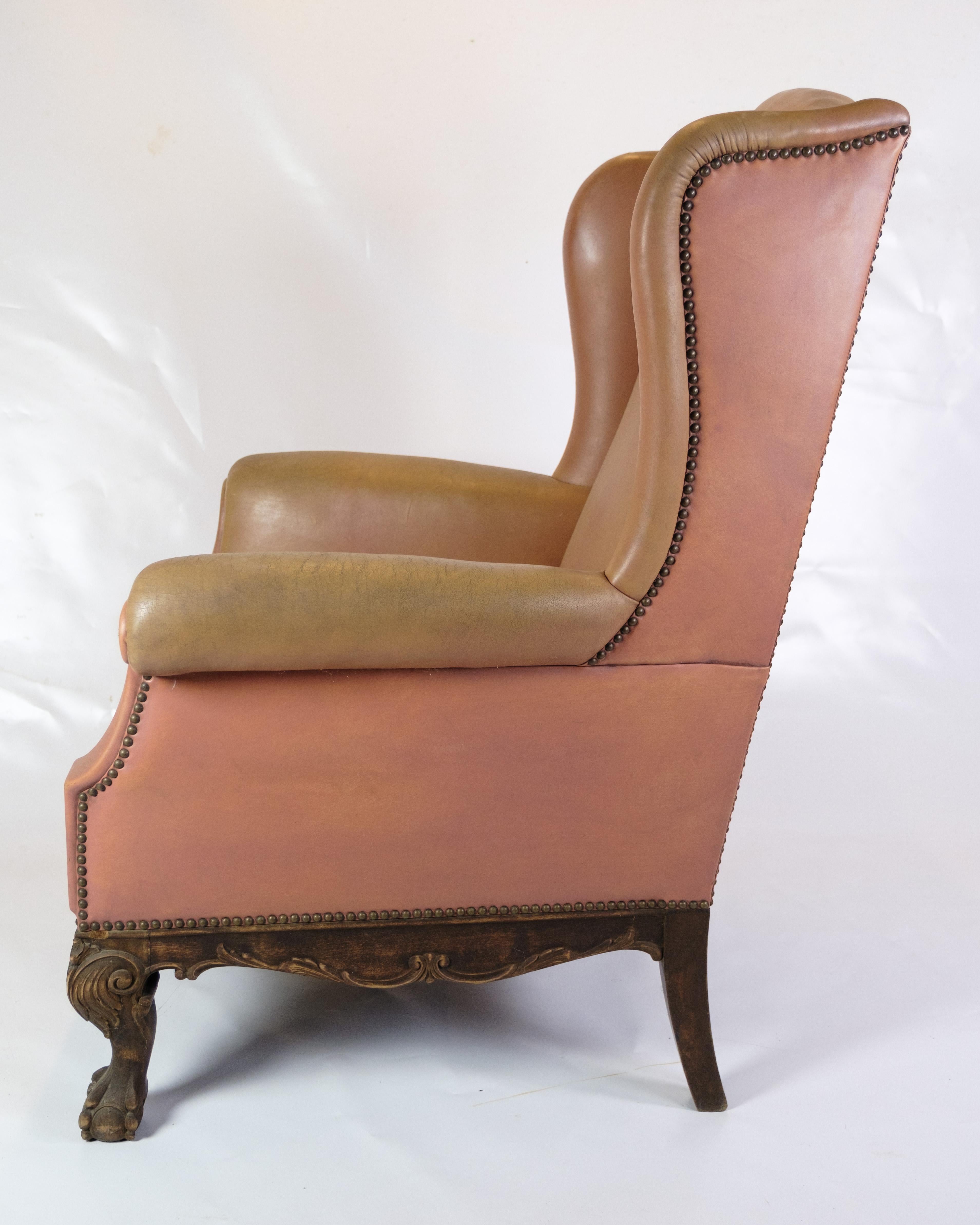 Cette chaise ancienne à hauts abattants de style Chesterfield est un chef-d'œuvre de l'art mobilier des années 1920. Tapissé de cuir marron clouté, ce fauteuil dégage une élégance et une sophistication intemporelles, caractéristiques du design