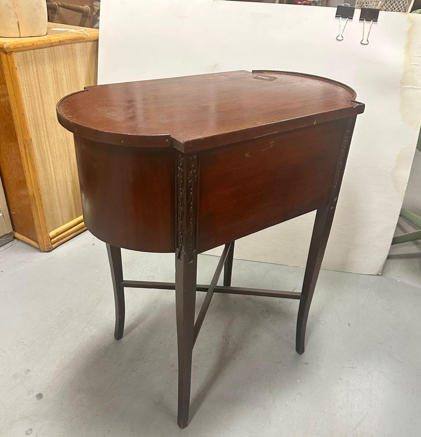 This antique regency end table with a federal-inspired shape is made with dark mahogany and has a unique shape that will complete in any direction. There are two cabinets. There is an ornate motif on the corners of the table. This table does have