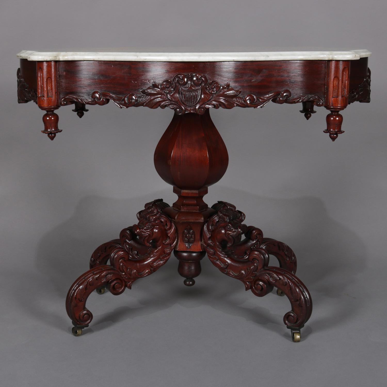 Antique high Victorian centre table features shaped and bevelled marble turtle top seated on carved rosewood base with skirt having central carved foliate with shield design and corner drop finials above faceted gourd from plinth raised on four