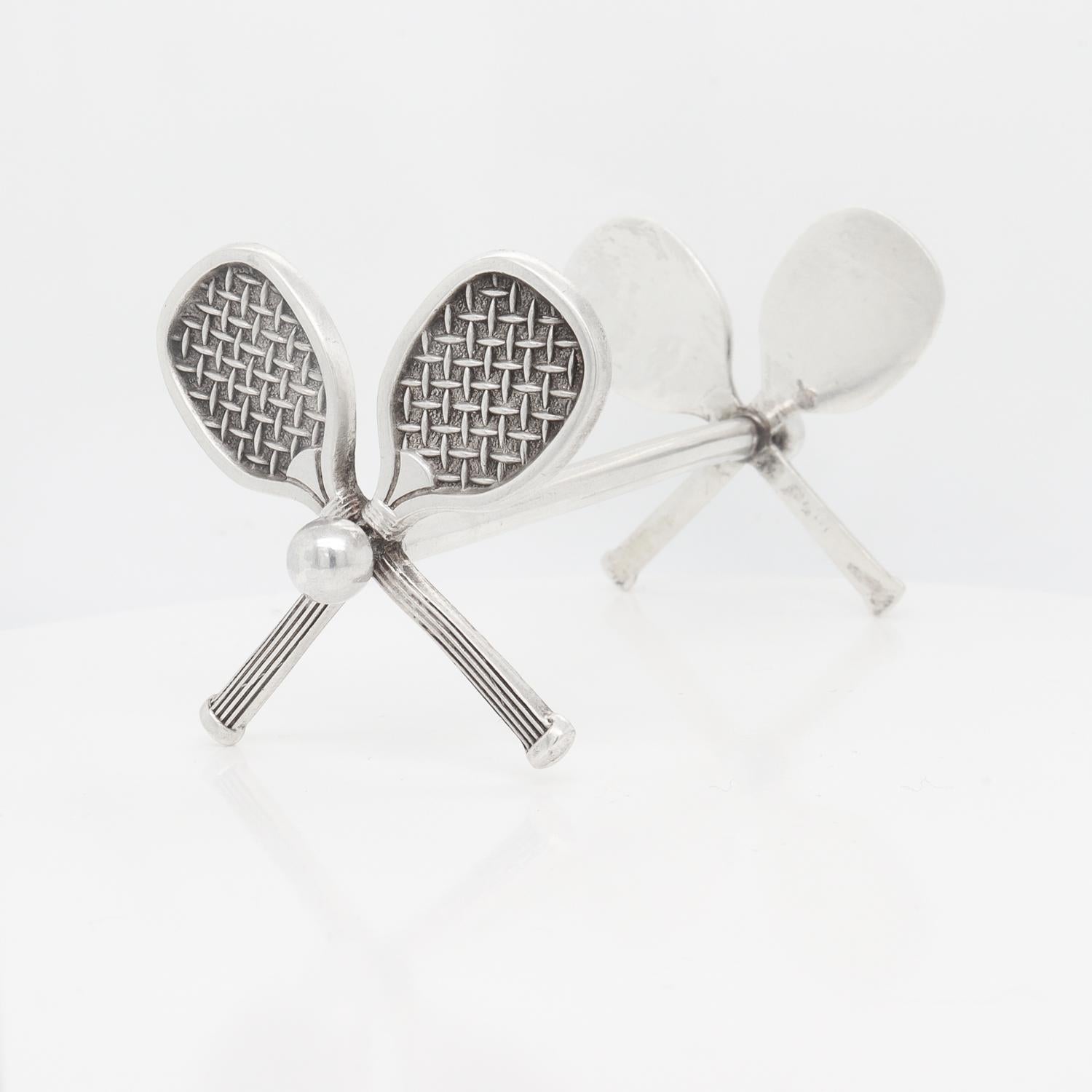 Un fino reposacuchillos figurado antiguo. 

En plata de ley.

De Hilliard & Thomason, los famosos fabricantes de objetos de plata de Birmingham, Inglaterra.

Cada extremo en forma de 2 raquetas de tenis cruzadas sostenidas por una barra central con