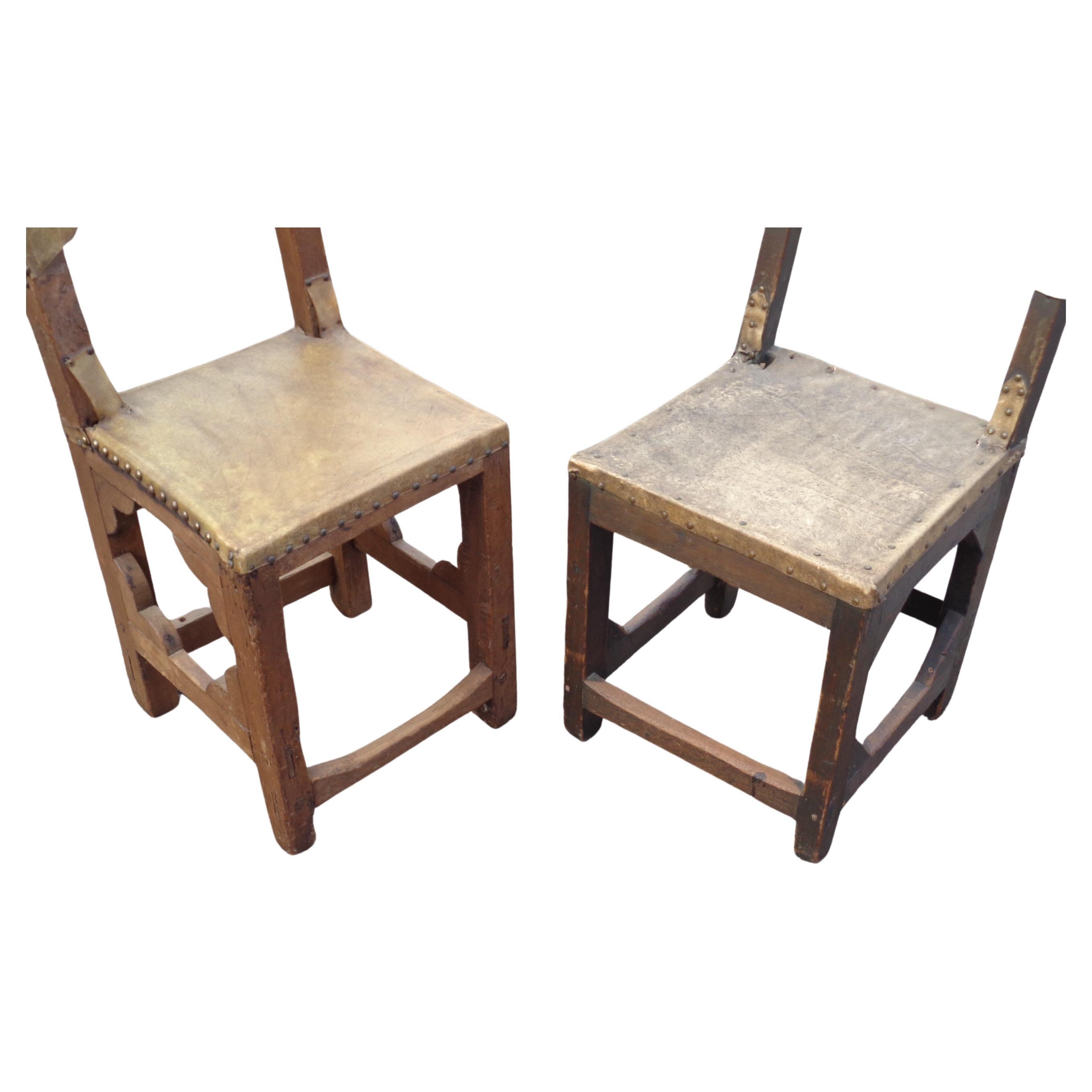 A near pair of antique rustic Spanish Colonial chairs. We think they are
 New Mexico / Mexico in origin. Hand carved early pegged and mortised joinery construction. Original brass metal tacked rare vellum hide seats and backs. One chair is hand